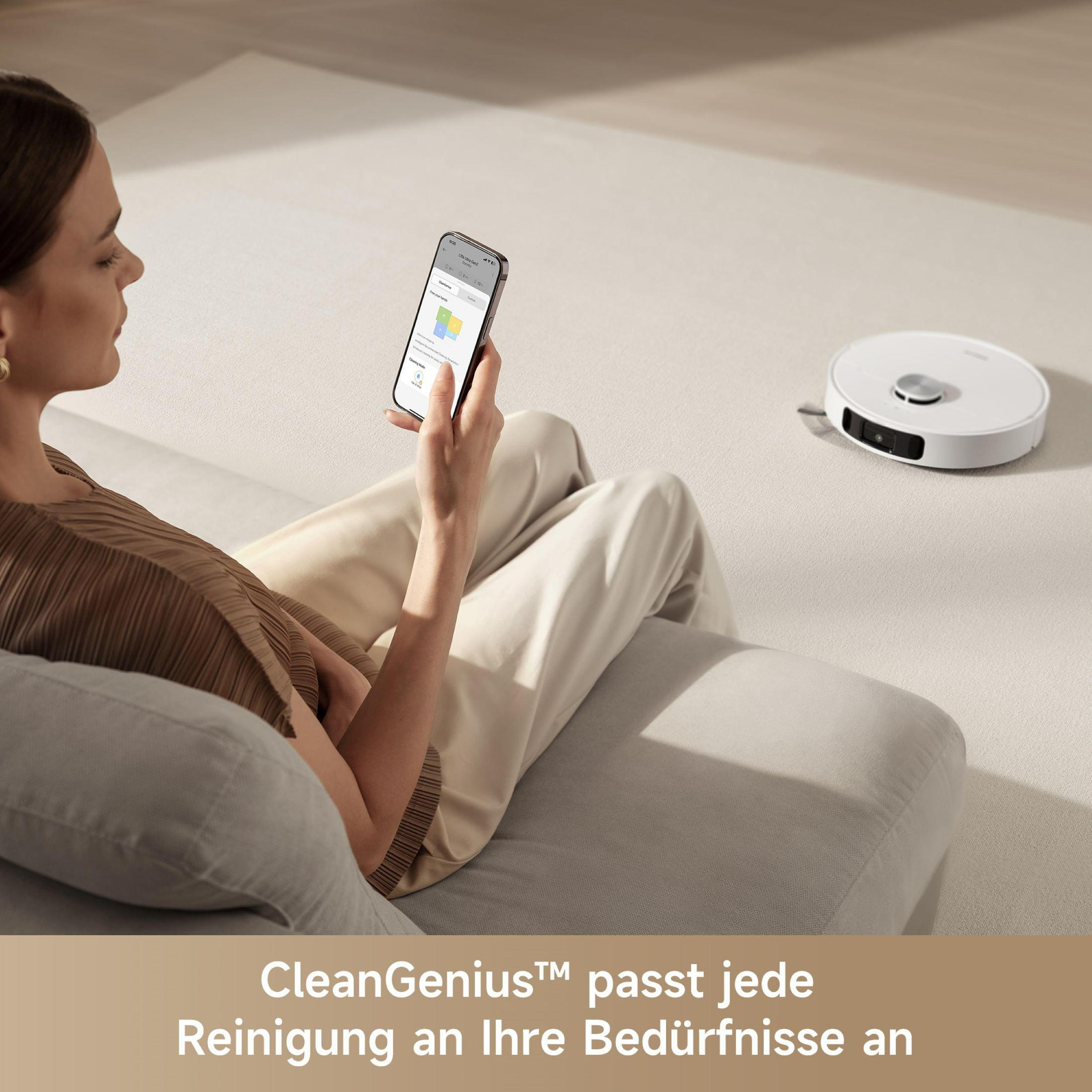 Frau auf Couch mit Telefon, Roboter-Staubsauger auf dem Boden. Text: CleanGenius™ passt sich jedem Reinigungsbedürfnis an.