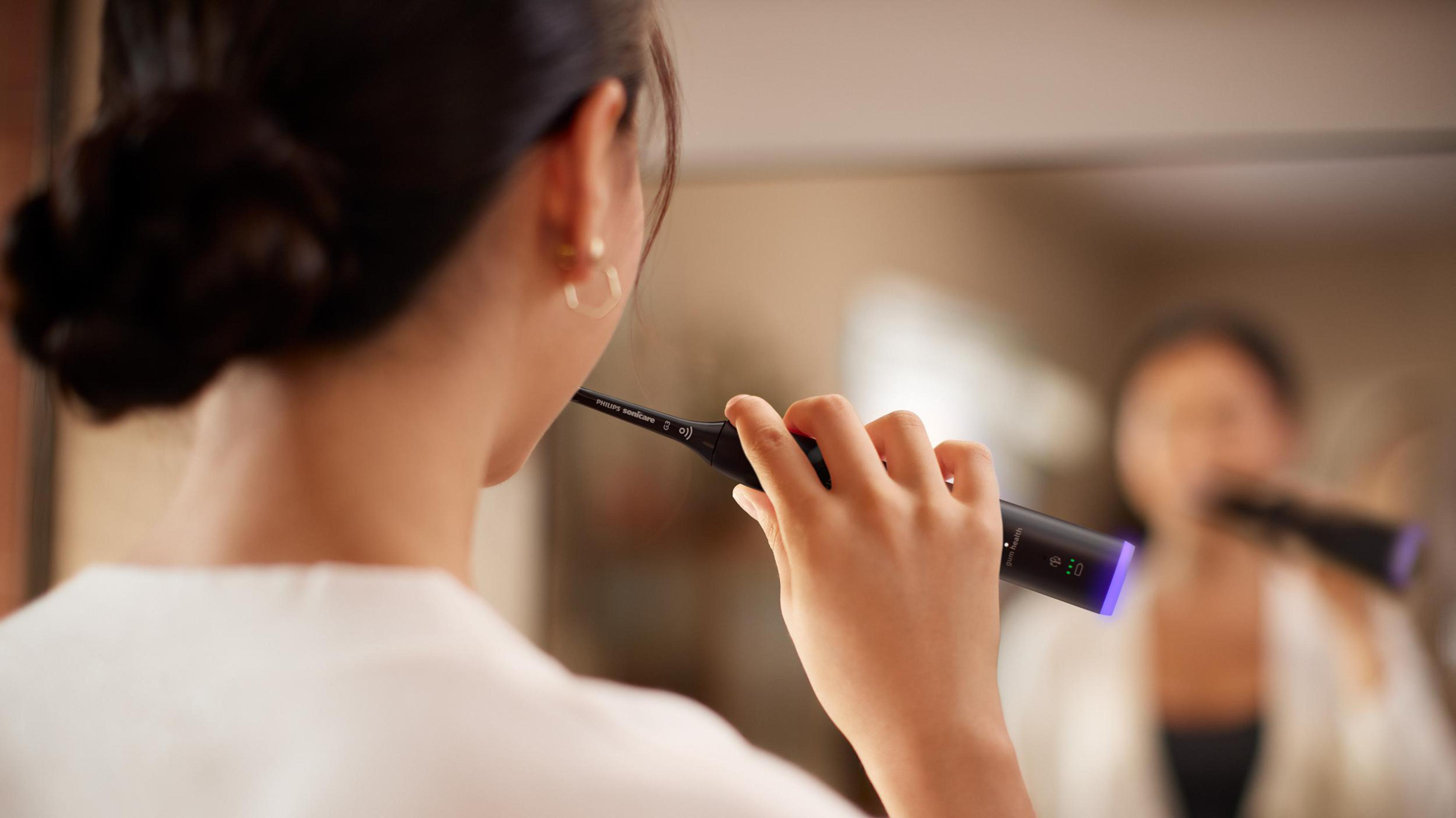 Osoba myjąca zęby szczoteczką elektryczną, odbicie w lustrze.