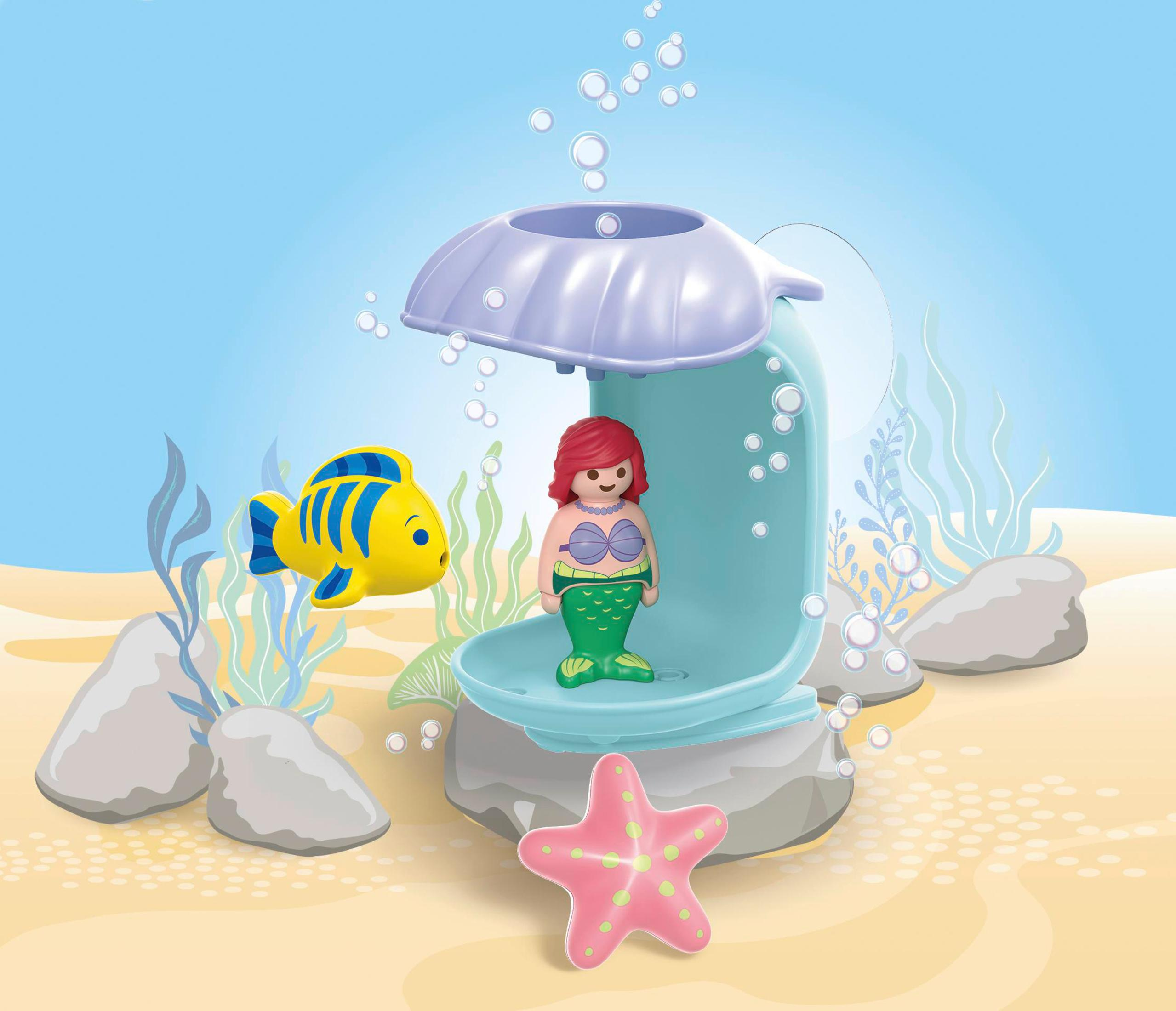Ein Meerjungfrau-Spielzeug in einer Muschel mit einem gelben Fisch und einem rosa Seestern.