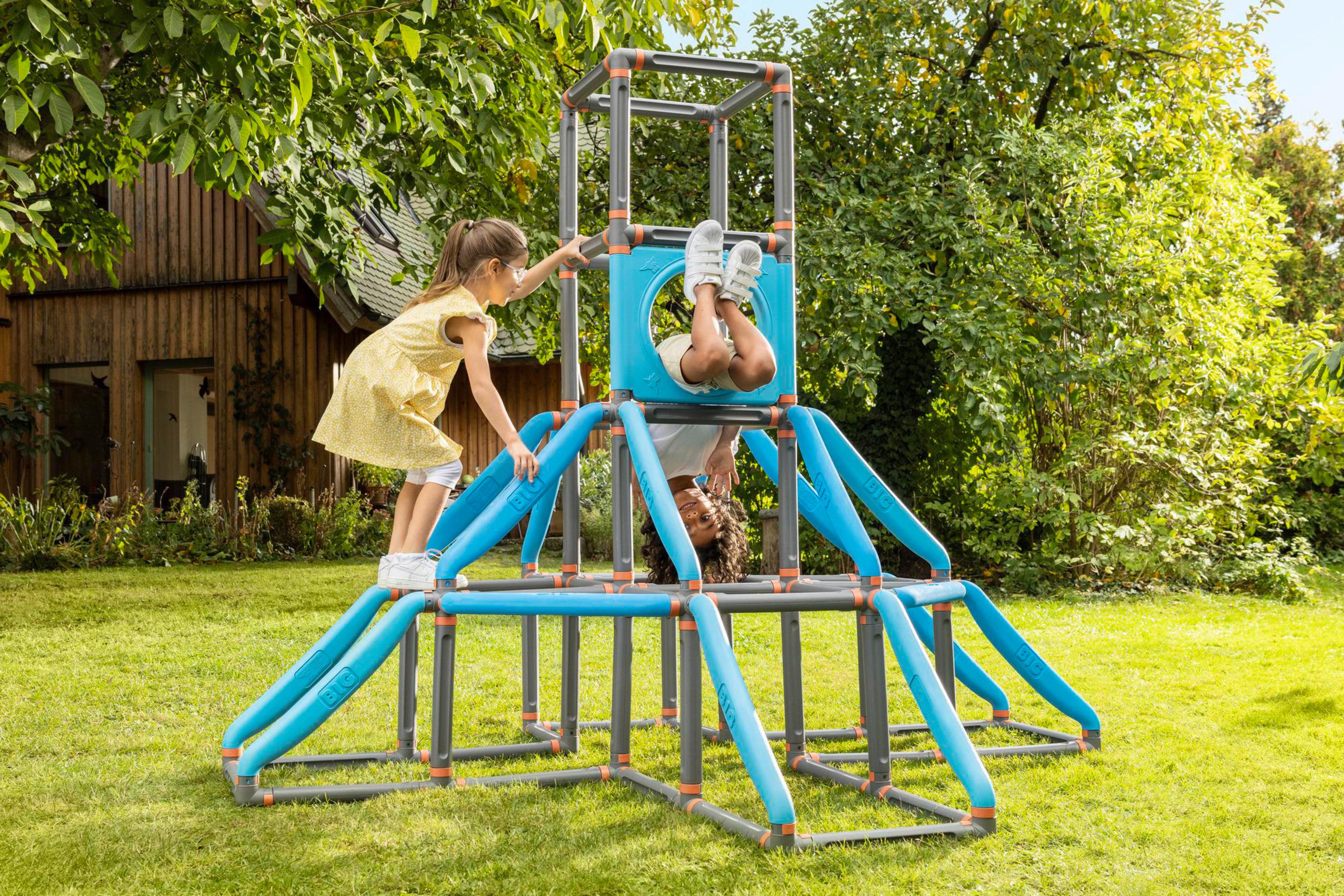 Zwei Kinder spielen auf einem blau-grauen Klettergerüst in einem grünen Garten mit Bäumen.
