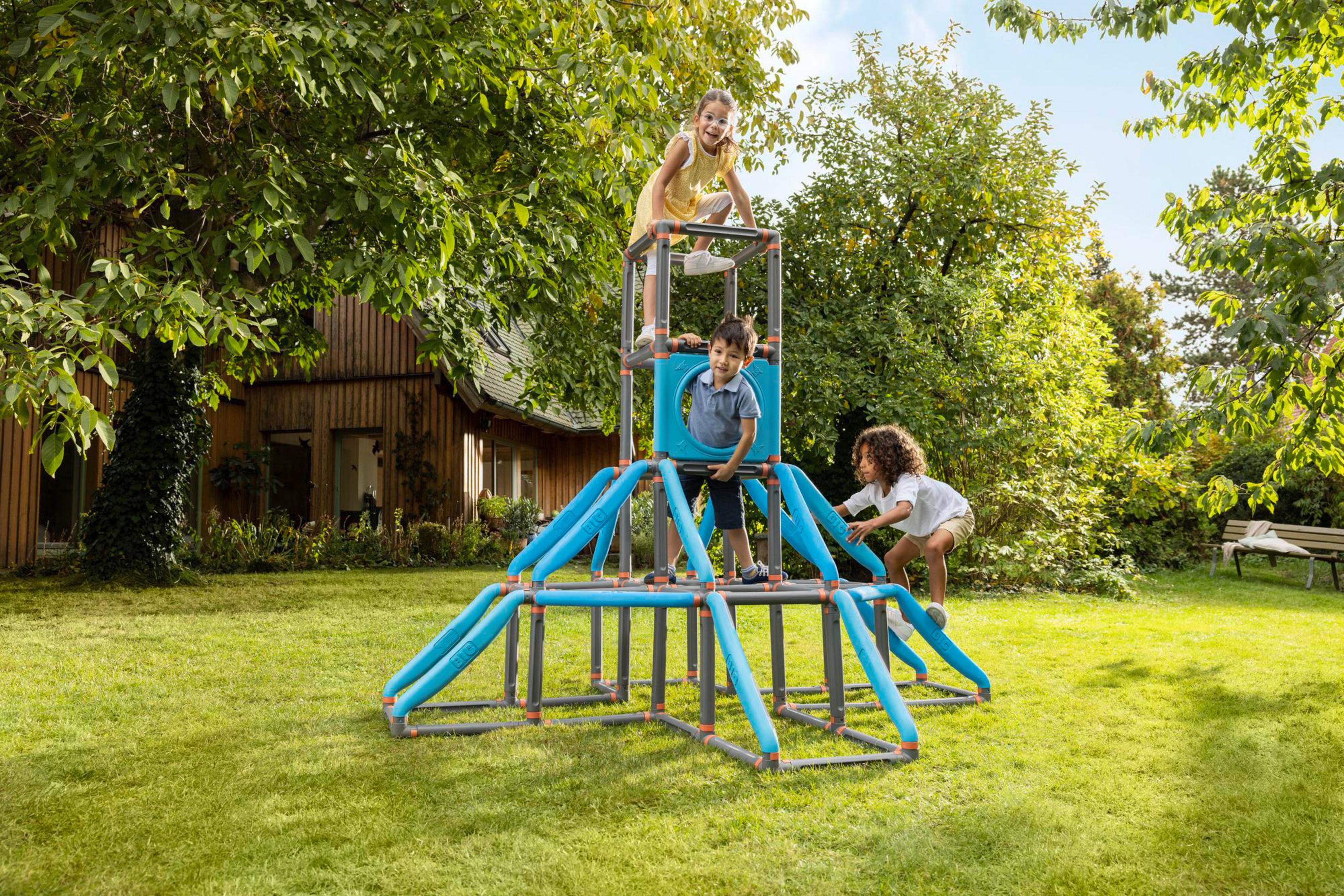 Kinder spielen auf einem Spielplatz-Gerüst im Garten. Grünes Gras, Bäume und ein Haus sind sichtbar.