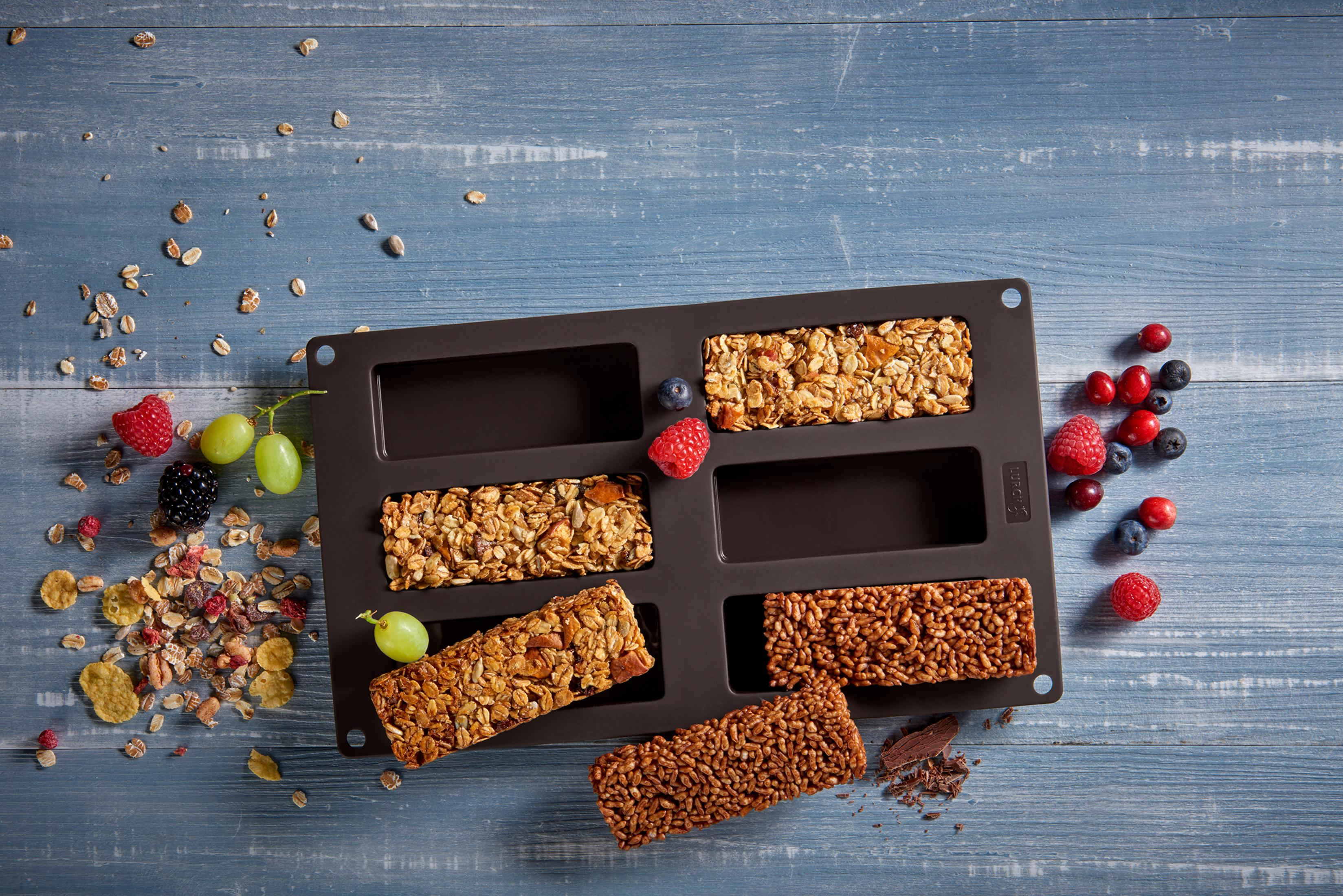 Batony zbożowe na tacy. Niebieskie drewniane tło. Rozrzucone jagody i orzechy.