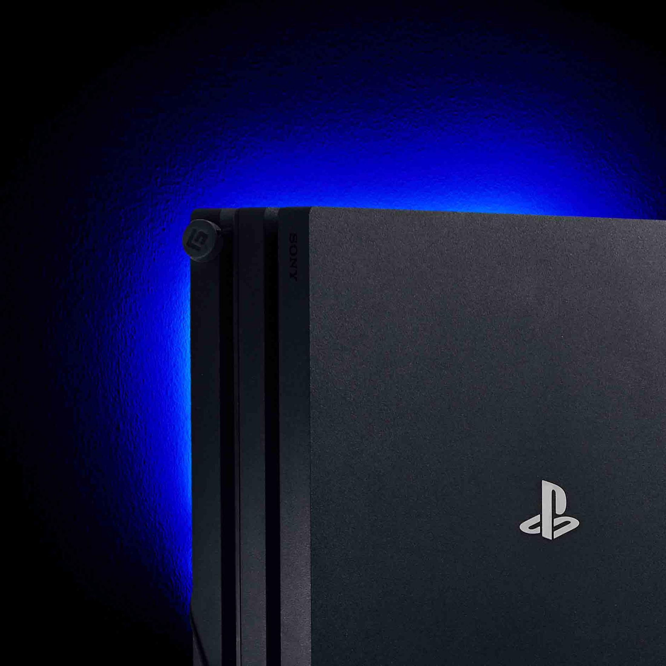 Nahaufnahme einer schwarzen PlayStation-Konsole mit blauem Licht. Sony-Logo sichtbar. Dunkler Hintergrund.