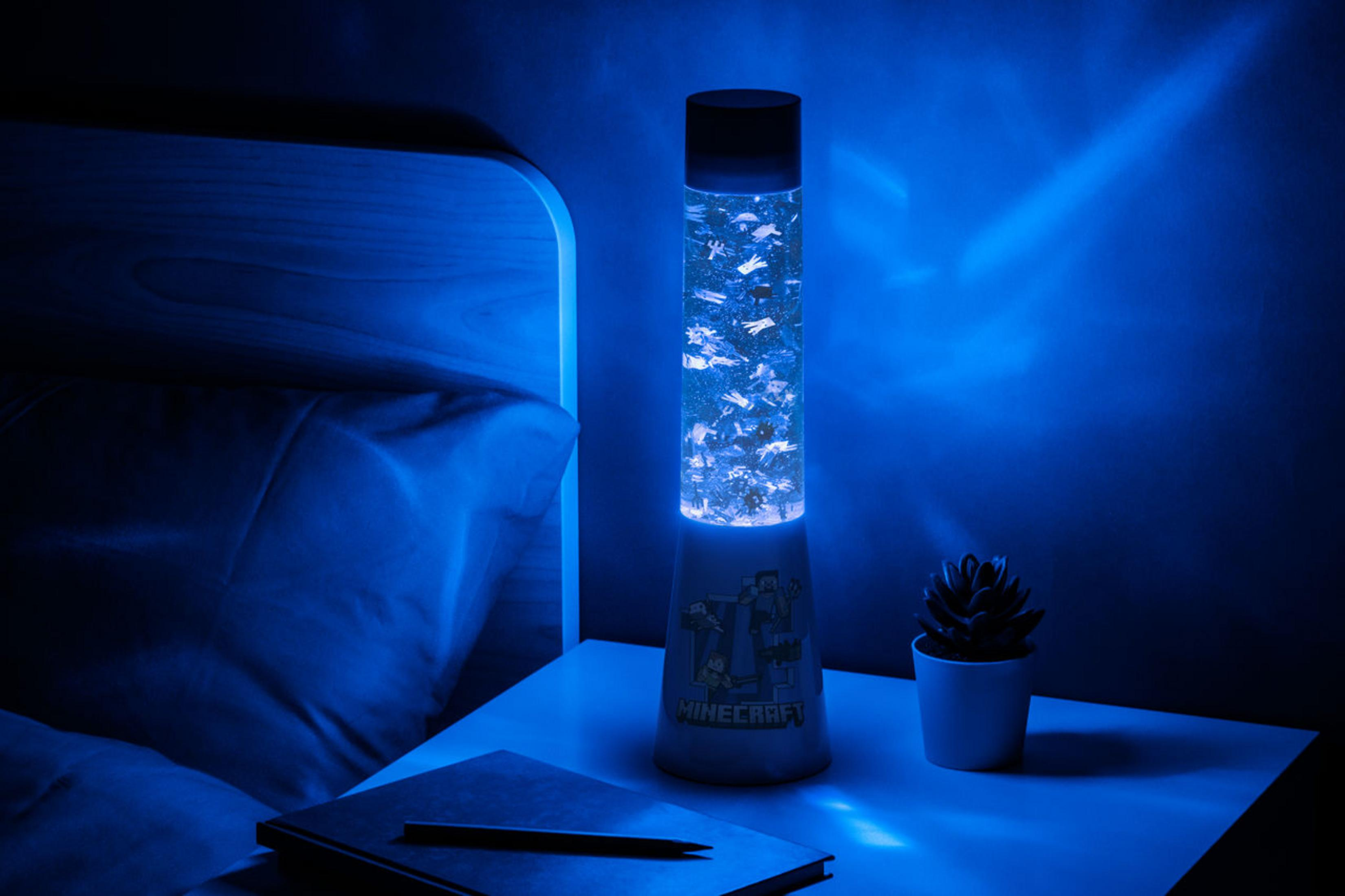 Una lámpara temática de Minecraft en una mesita de noche, brillando en azul, con un libro y una planta.