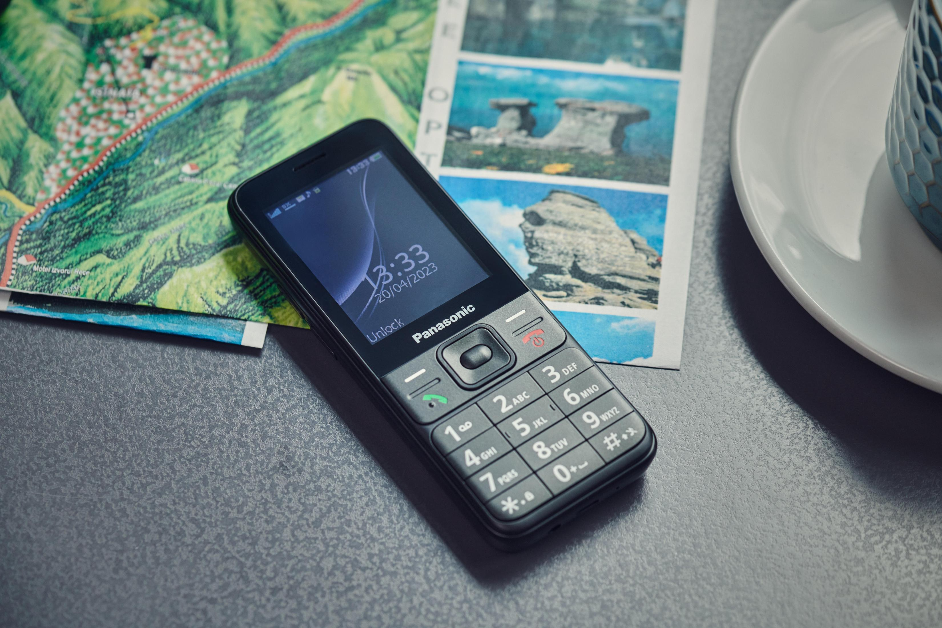Schwarzes Panasonic-Telefon auf einer Karte und einem Bild, zeigt Zeit und Datum.