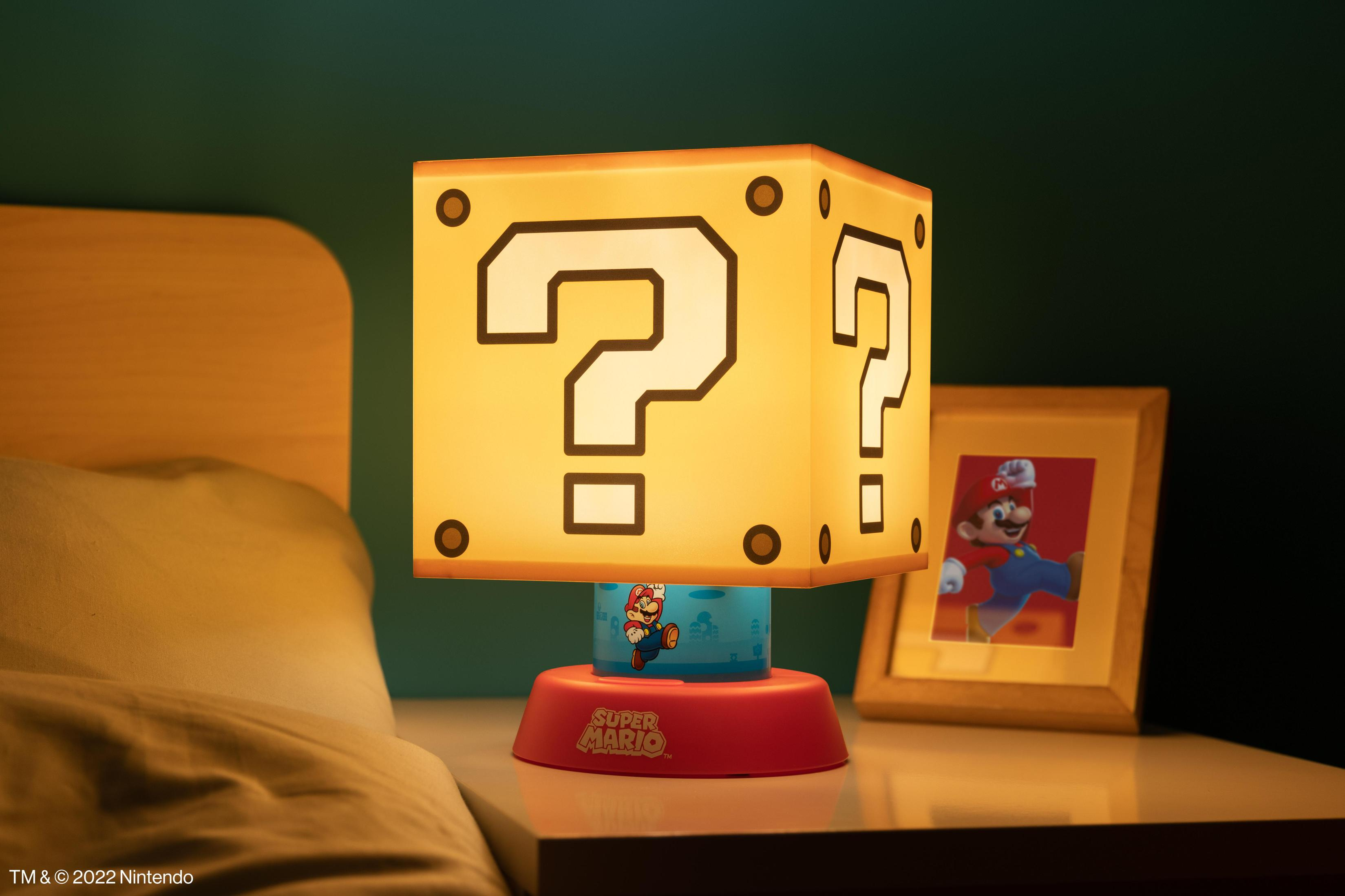 Lampa z blokiem znaku zapytania Super Mario z figurką Mario na czerwonej podstawie. W pobliżu jest oprawiony obrazek.