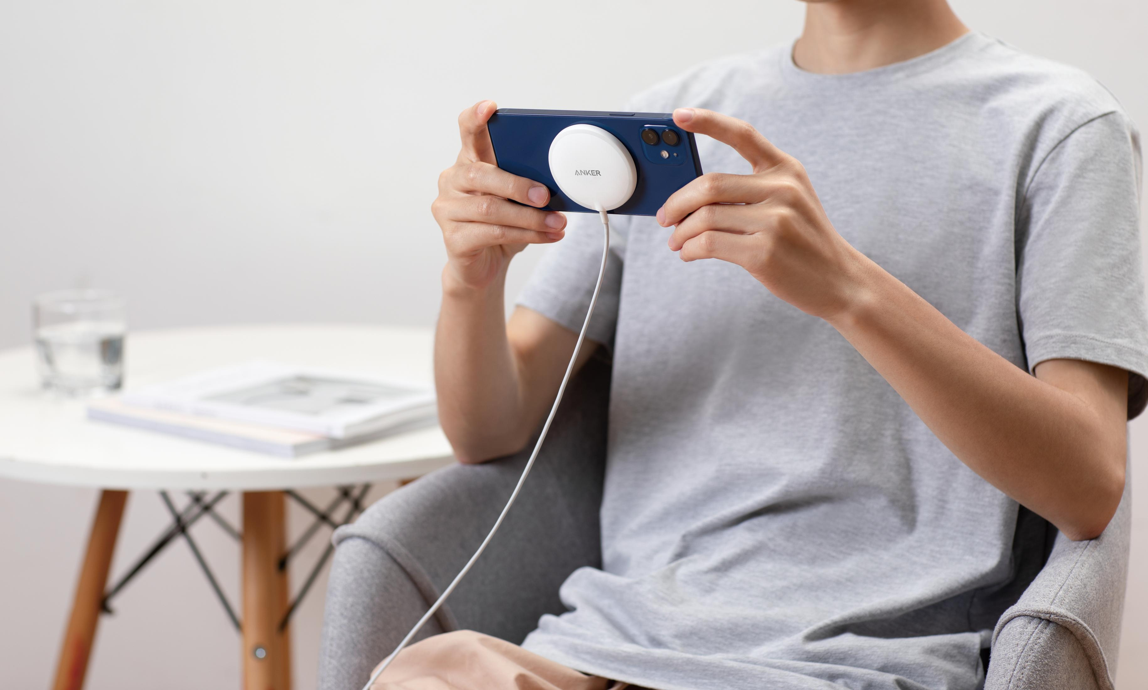 Persona che tiene un telefono con disco di ricarica, vicino a tavolo e bicchiere.
