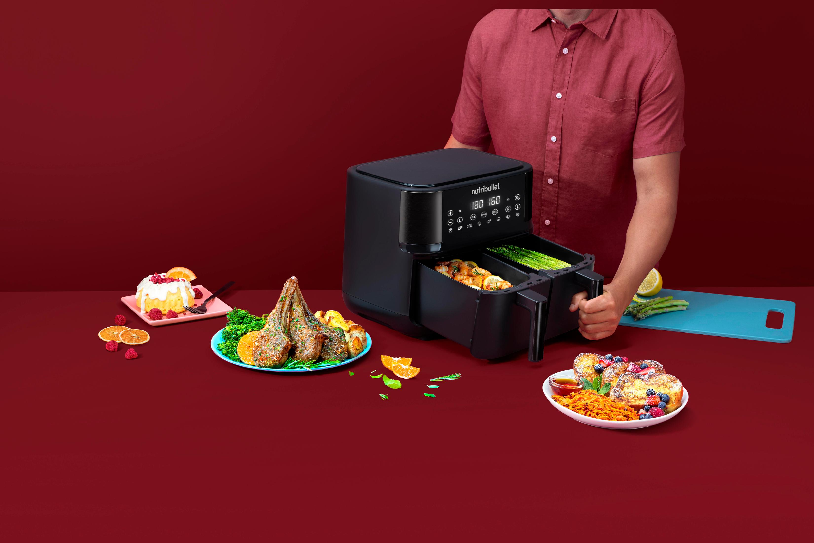 Czarna frytkownica powietrzna z jedzeniem dookoła. Osoba trzyma tacę.