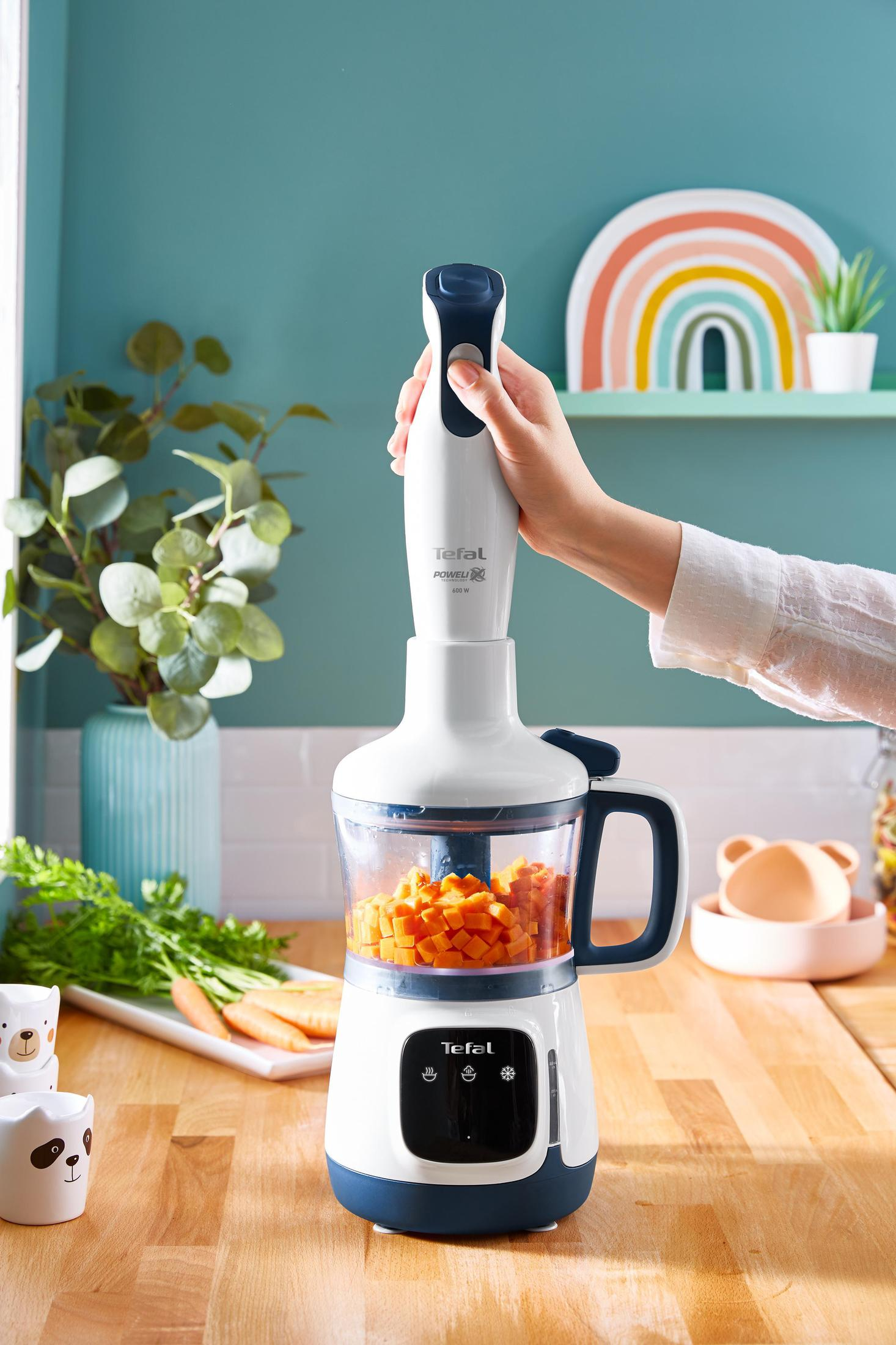 Un robot da cucina per bambini bianco e blu con carote e una mano che tiene il frullatore.