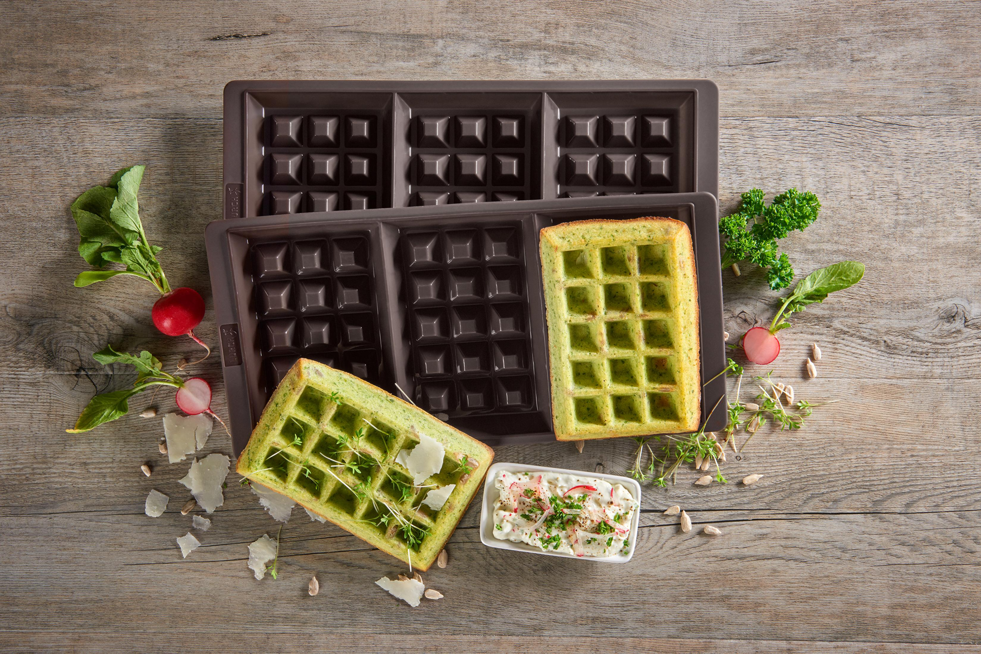 Dwie gofrownice z goframi, rzodkiewkami i ziołami. Jeden gofr jest w gofrownicy, drugi na talerzu.