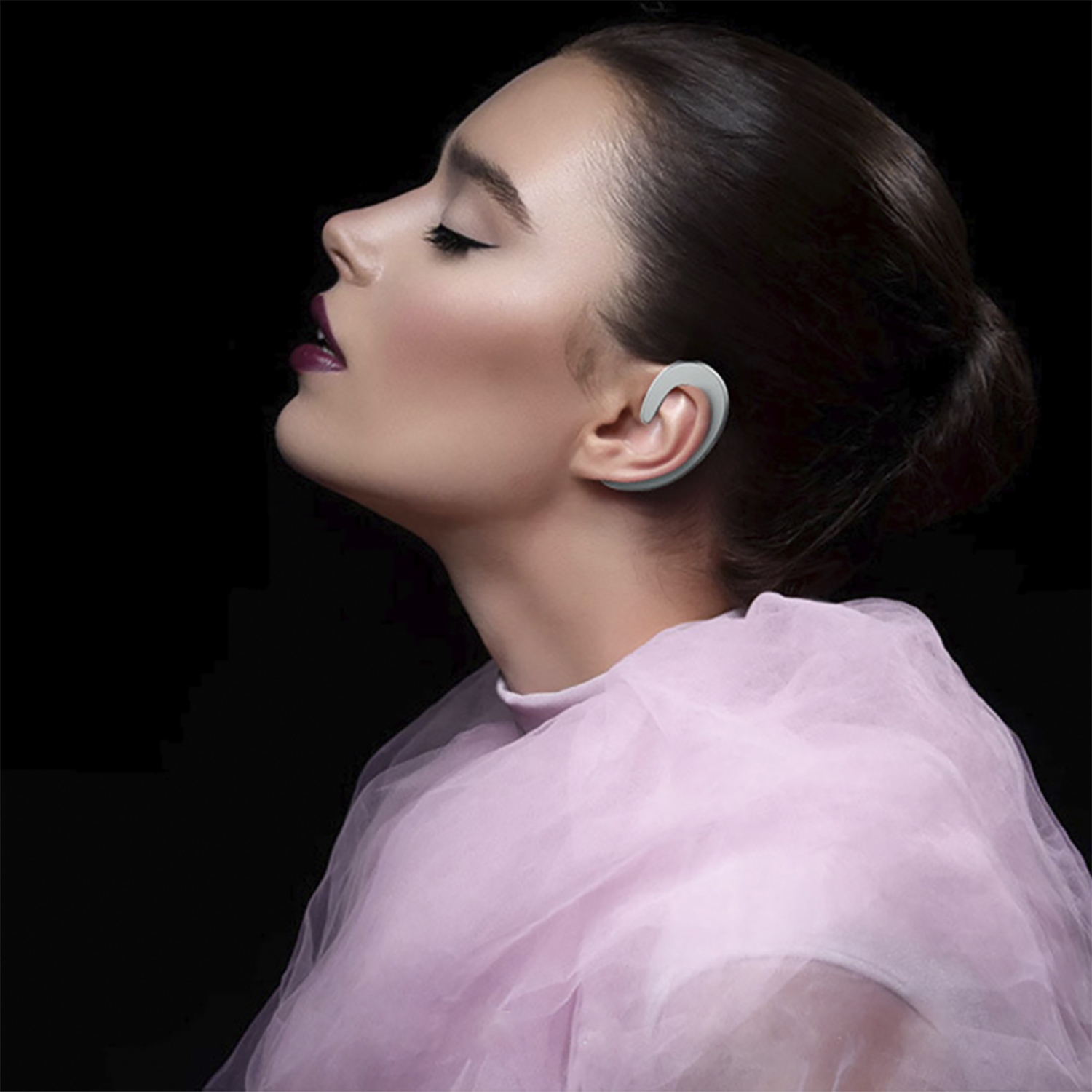 Una donna con un auricolare bianco. È di profilo e ha una sciarpa rosa.