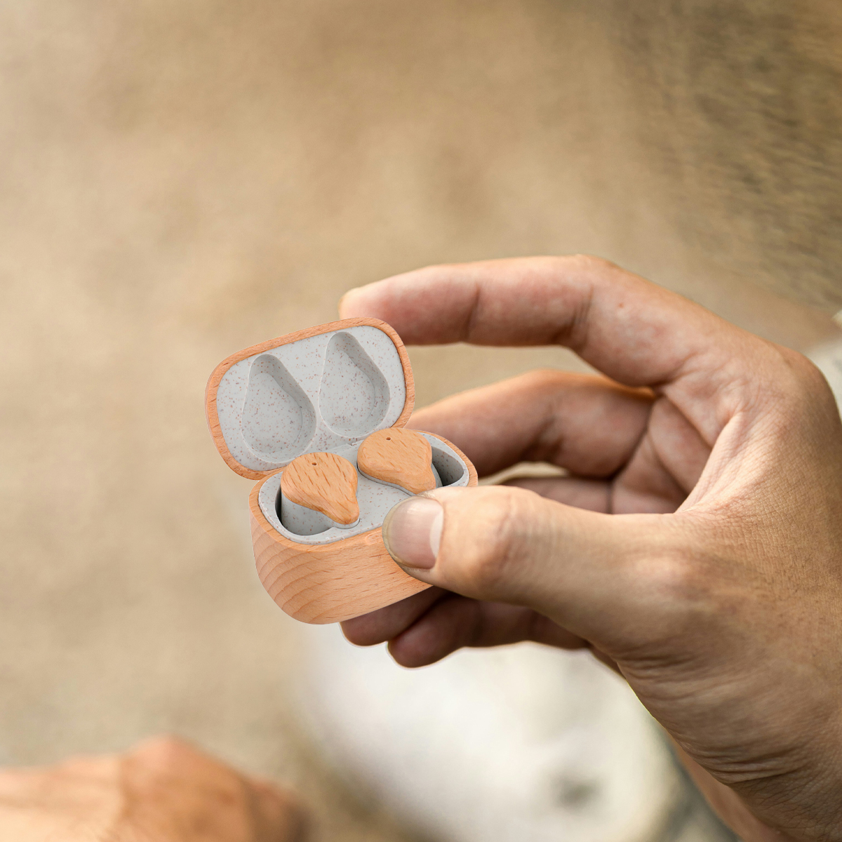 Auriculares en estuche, en la mano. Estuche y auriculares son de color naranja-marrón.