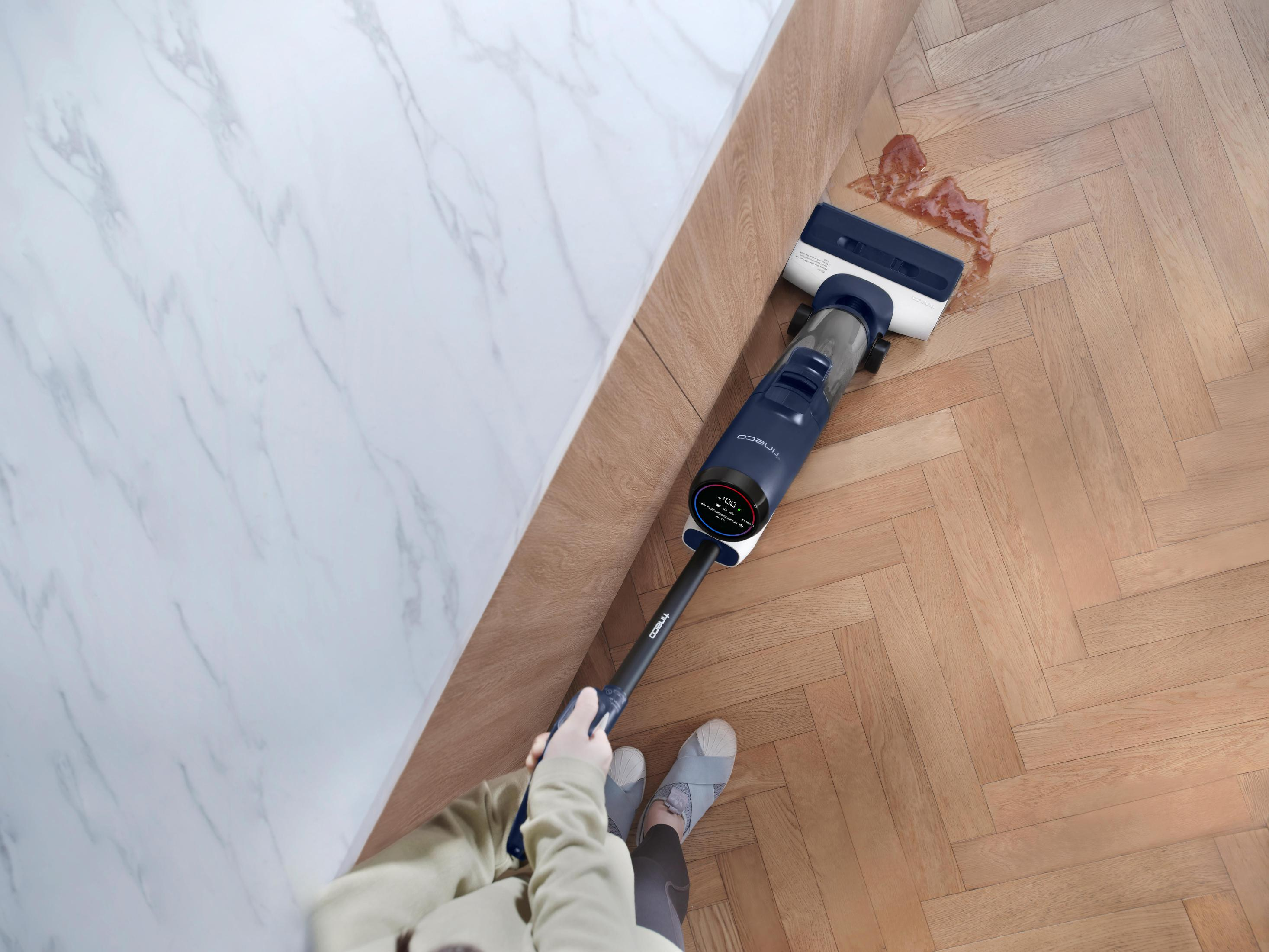 Osoba czyszcząca drewnianą podłogę za pomocą bezprzewodowego odkurzacza. Na podłodze jest rozlane.