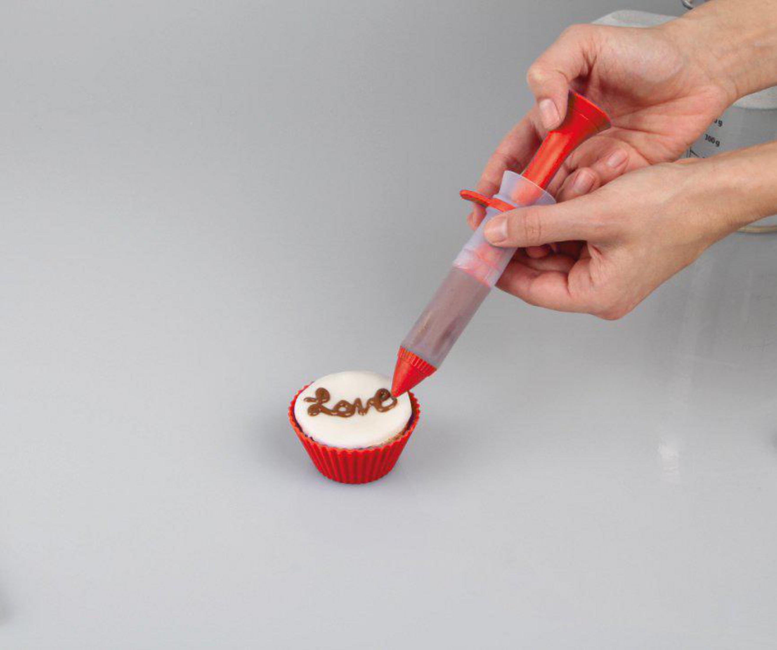 Person dekoriert einen Cupcake mit einer roten Spritztülle. Das Wort 'Love' steht auf dem Cupcake.