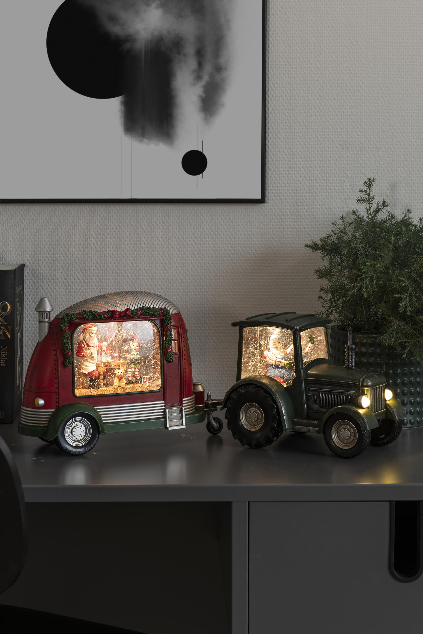 Roter Anhänger und grüner Traktor Weihnachtsdekorationen auf grauer Oberfläche, mit einem Gemälde im Hintergrund.