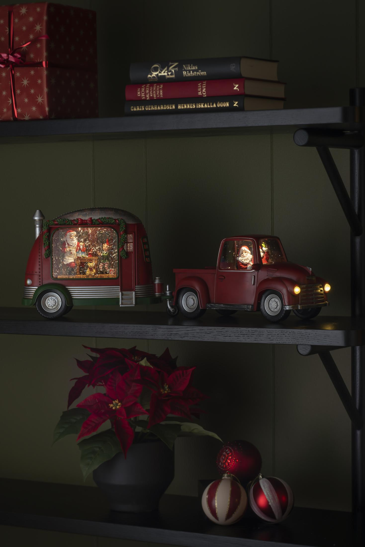 Weihnachtsausstellung mit rotem LKW und Anhänger auf einem Regal mit Weihnachtsdeko, Büchern und Pflanzen.