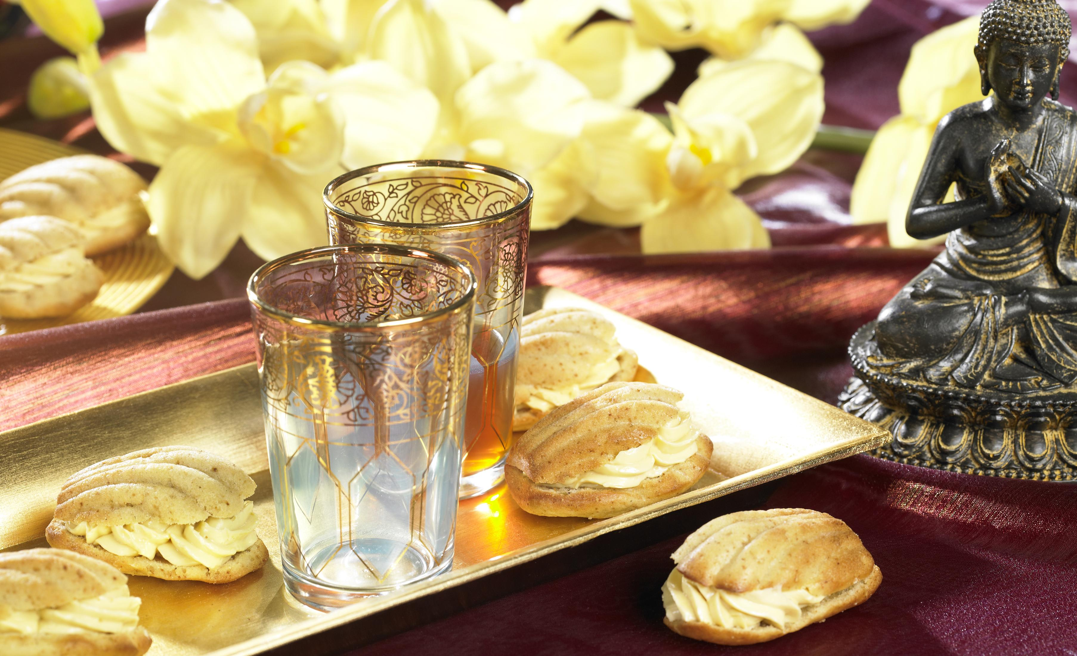 Złota taca z dwoma szklankami i ciastkami. Złoty posąg Buddy w tle.