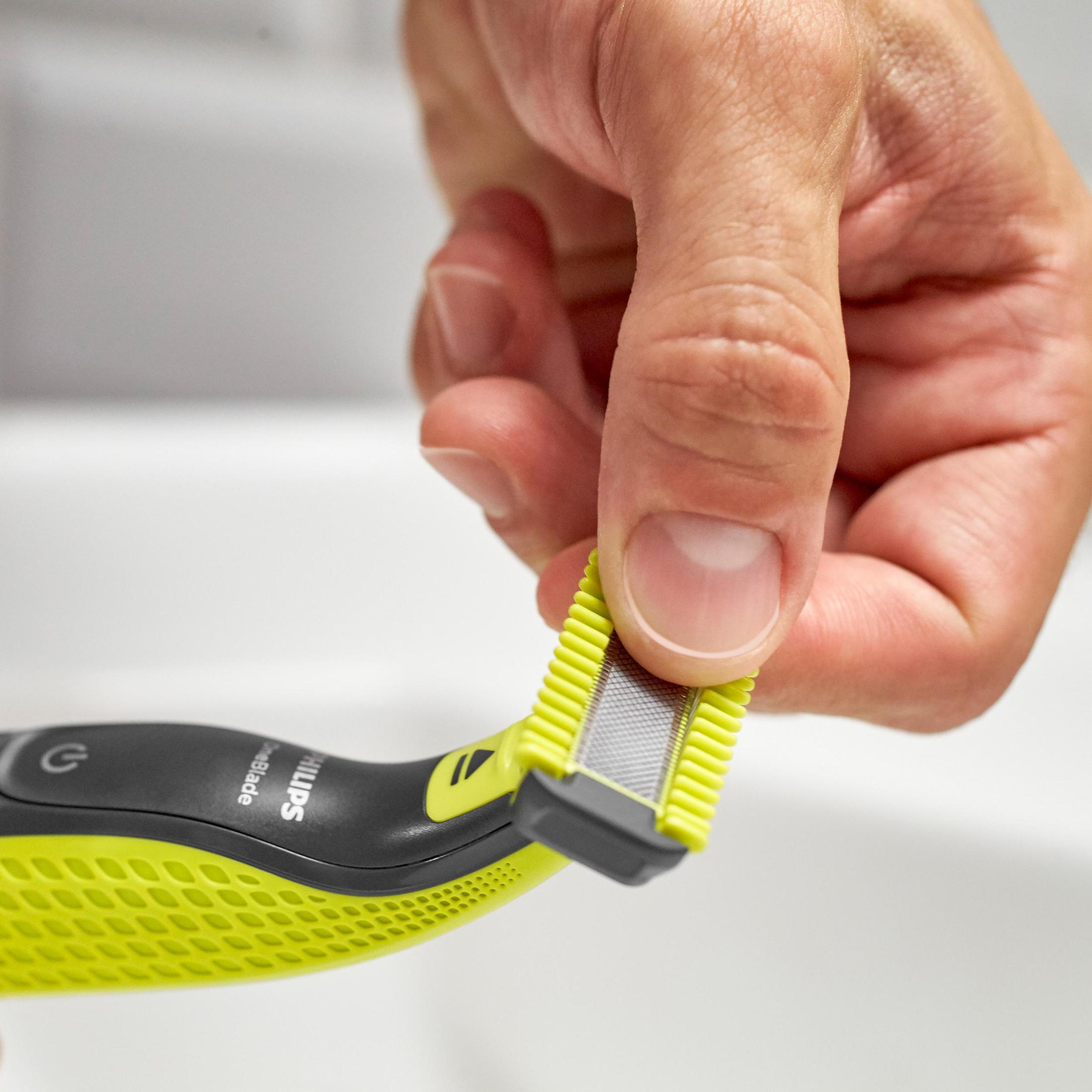 Dłoń trzymająca zielono-szarą golarkę Philips OneBlade, gotową do wymiany ostrza.