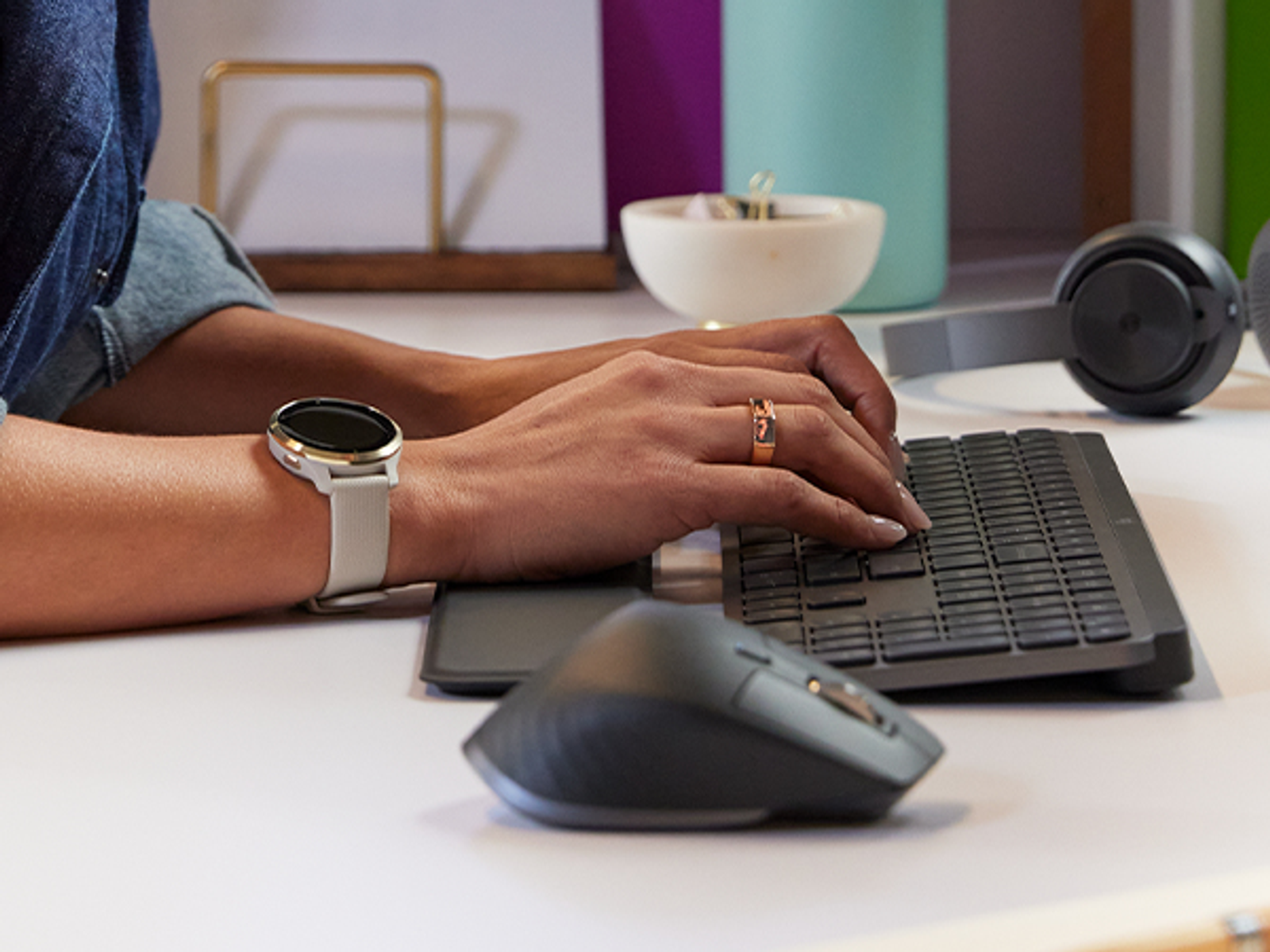 Osoba pisząca na klawiaturze, nosząca smartwatch i pierścionek, z myszą.