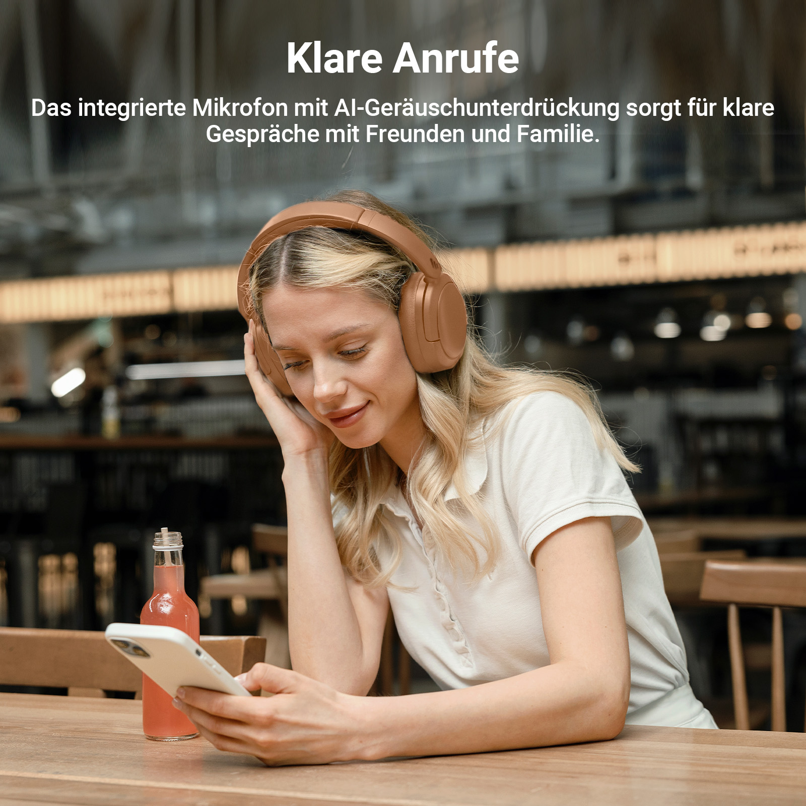 Frau mit Kopfhörern benutzt ein Handy am Tisch, eine Flasche Saft. Heller Hintergrund.