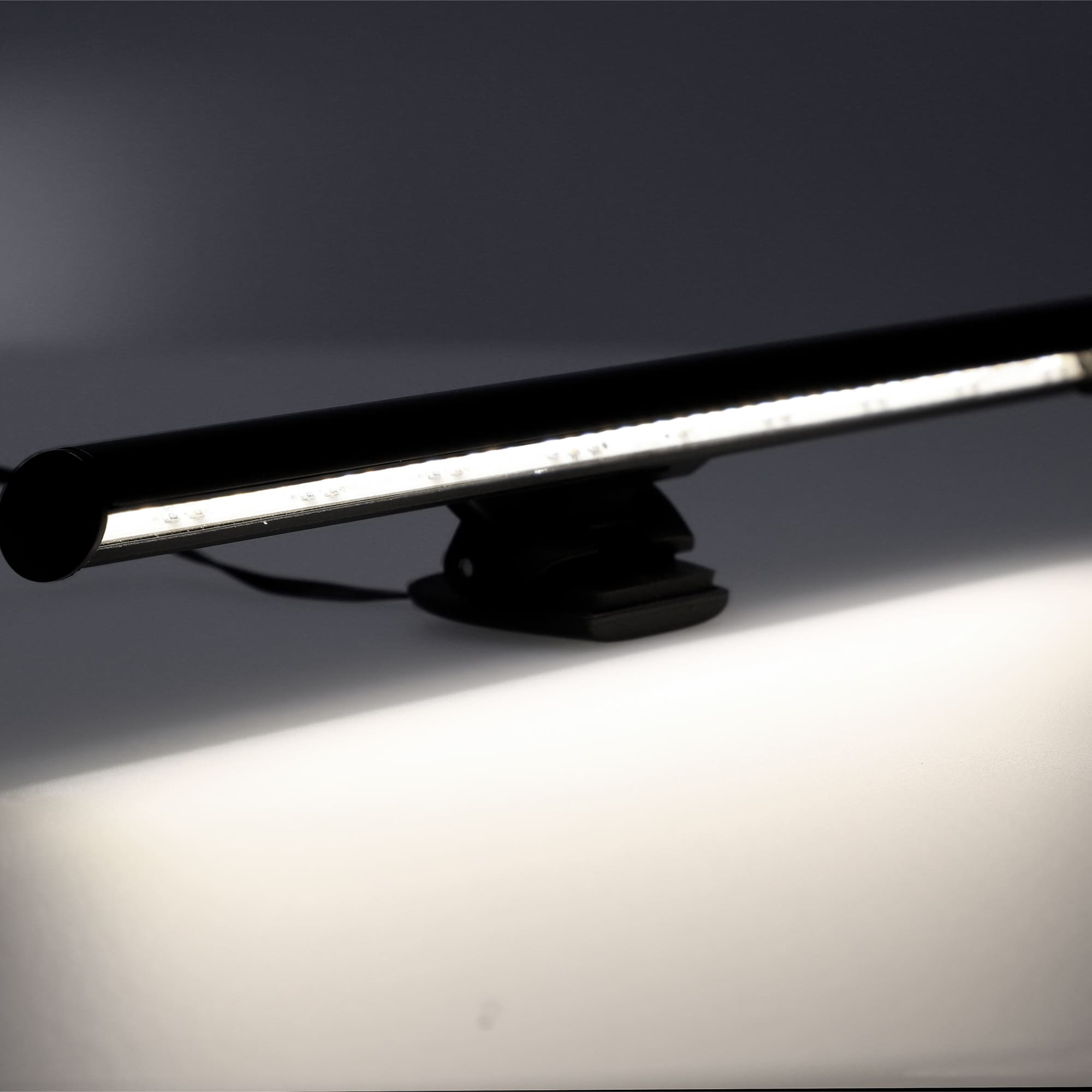 Lámpara de escritorio LED negra. Tiene un cuerpo largo y delgado y está montada sobre un clip.