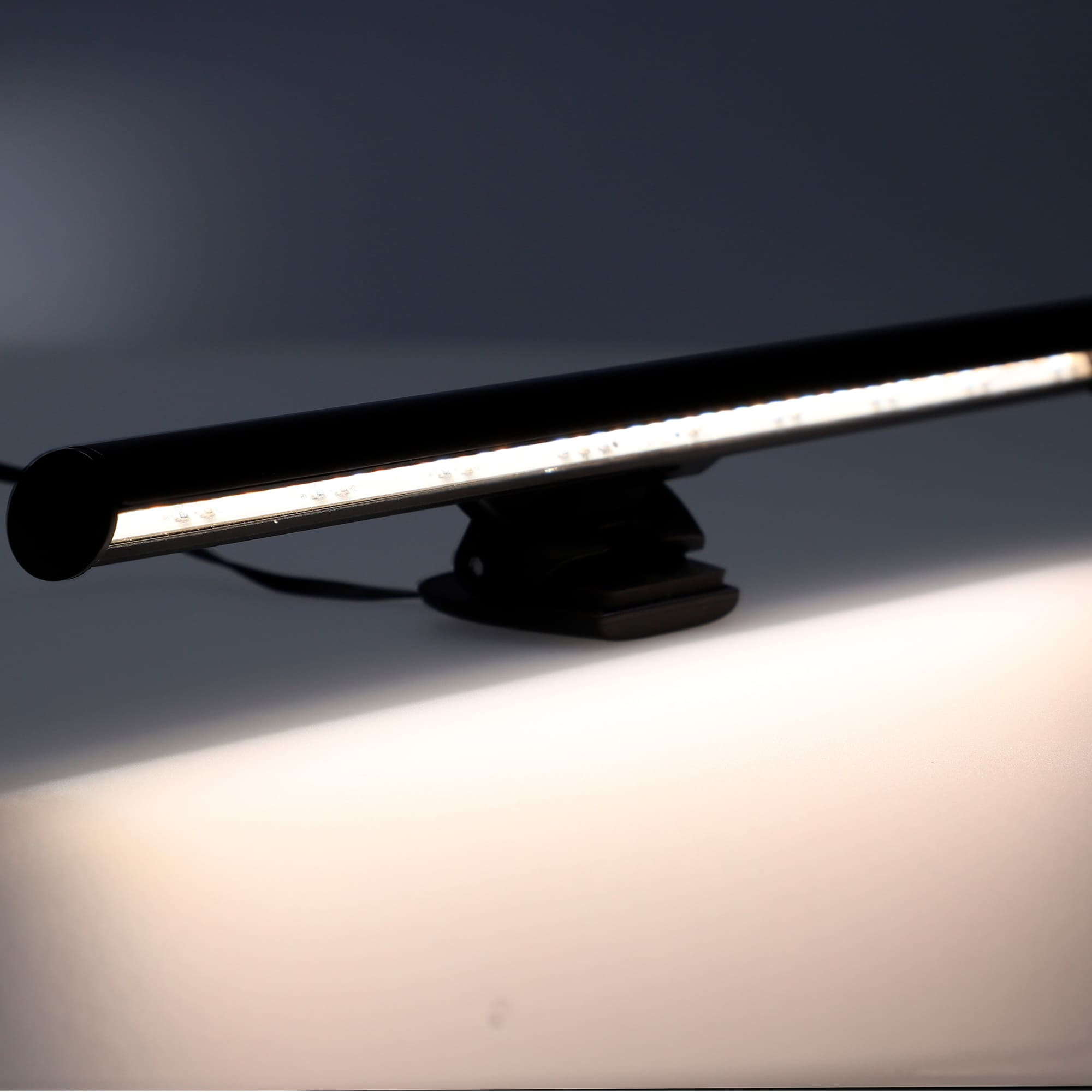 Barra de luz para monitor negra con luces LED blancas. La luz brilla sobre una superficie blanca.