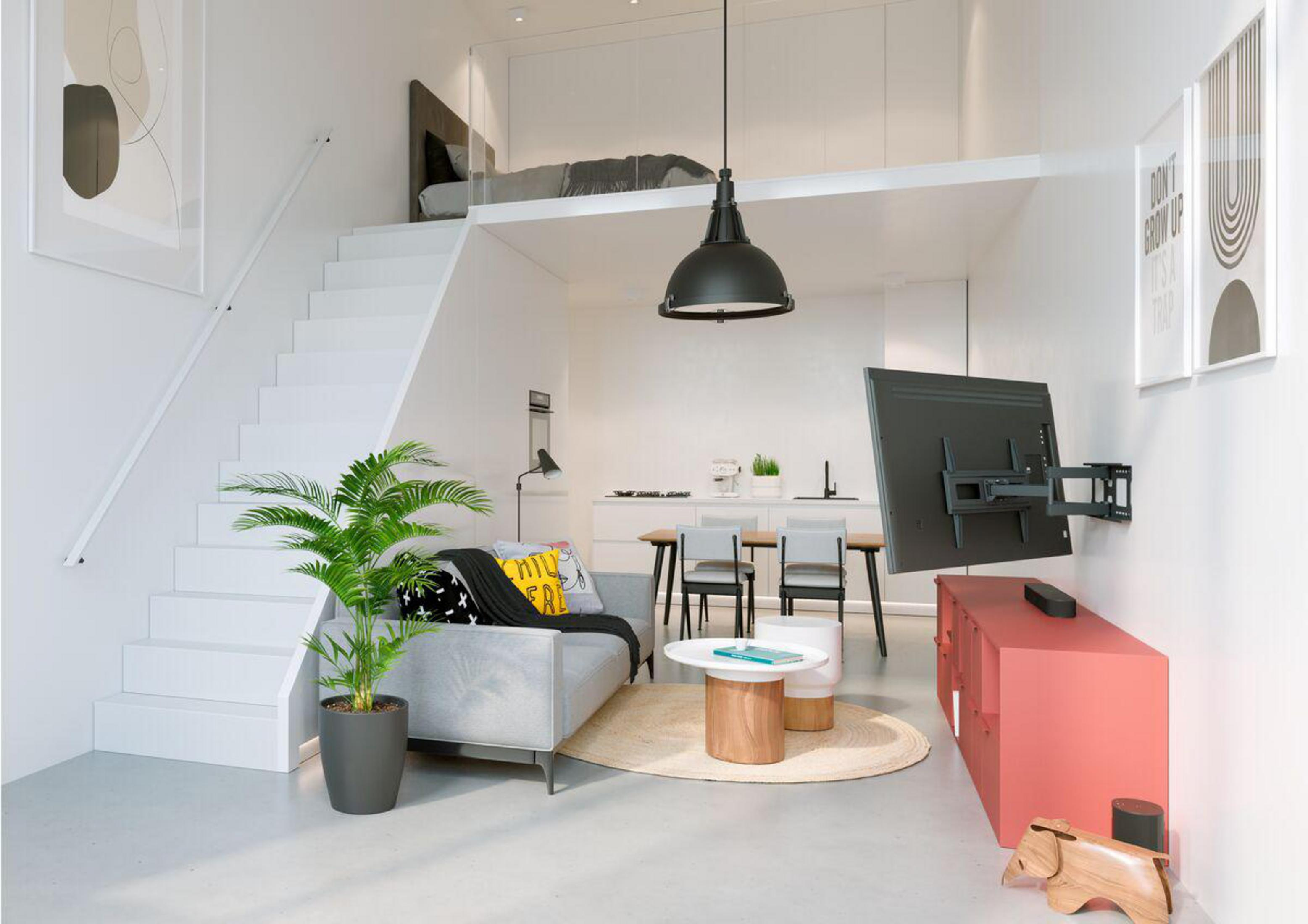 Salón moderno con cama alta, sofá, TV y decoración. Paredes blancas, suelos de madera y una planta complementan el diseño.
