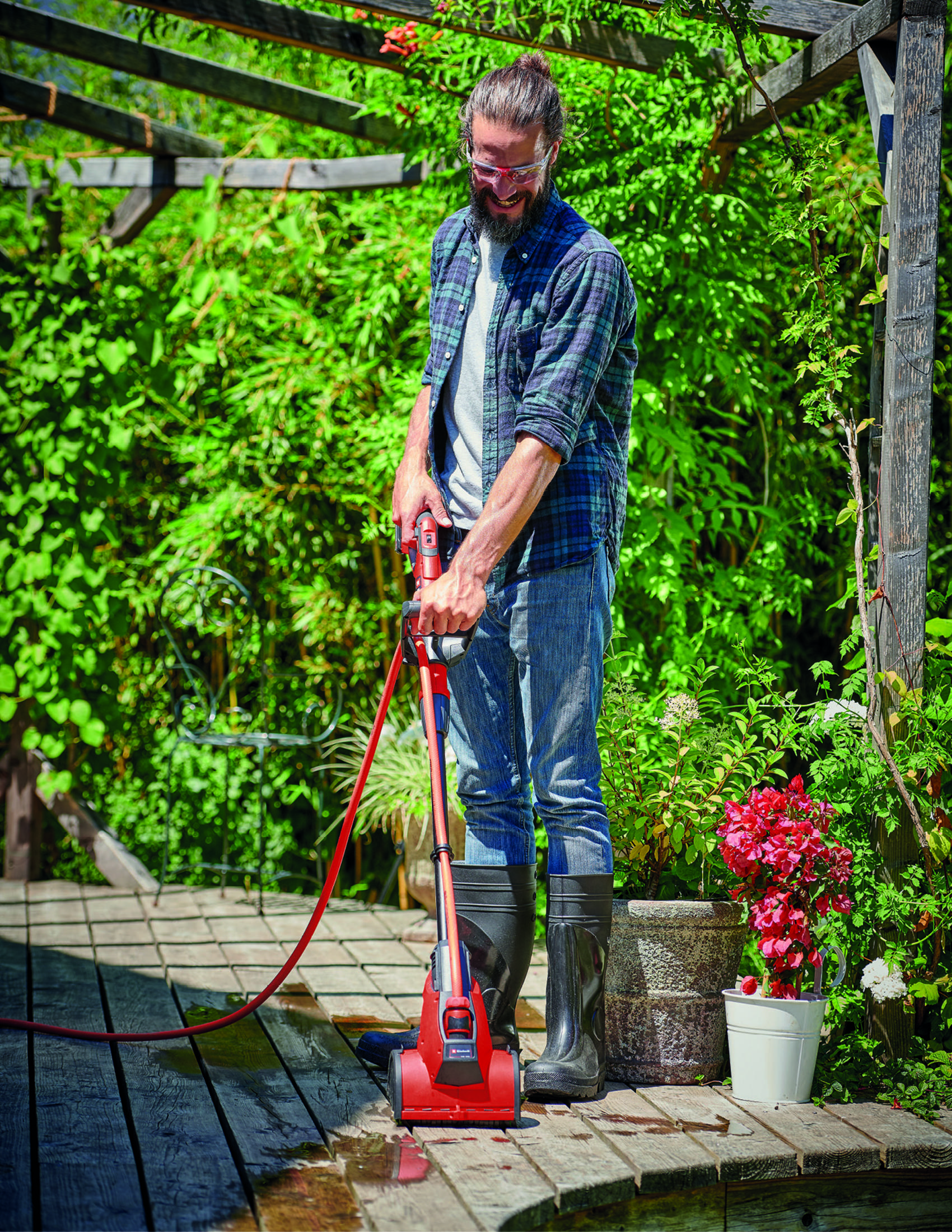 A man in a garden using a power washer on a wooden deck.