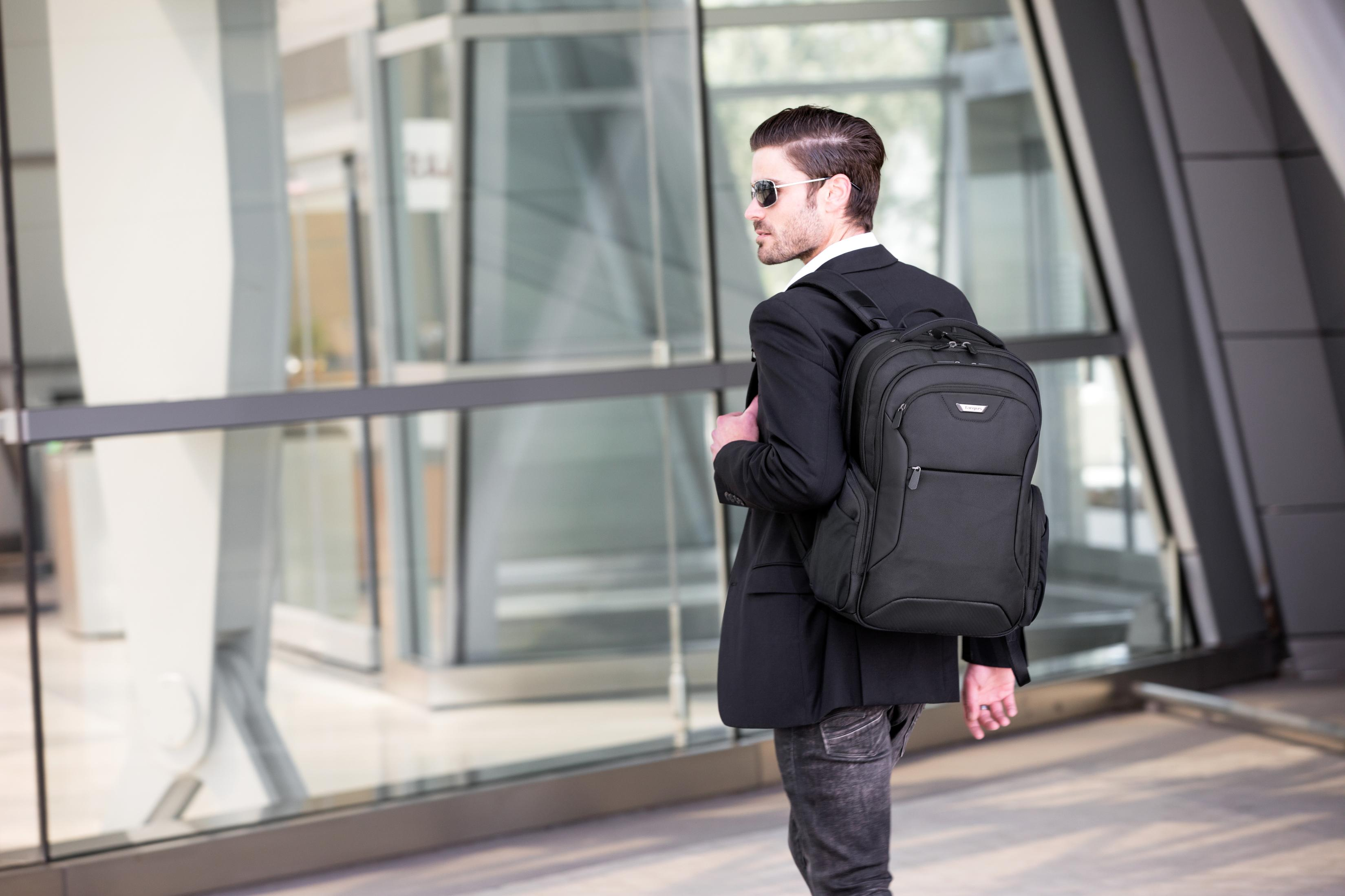 Ein Mann mit Sonnenbrille und Rucksack geht neben einer Glaswand.
