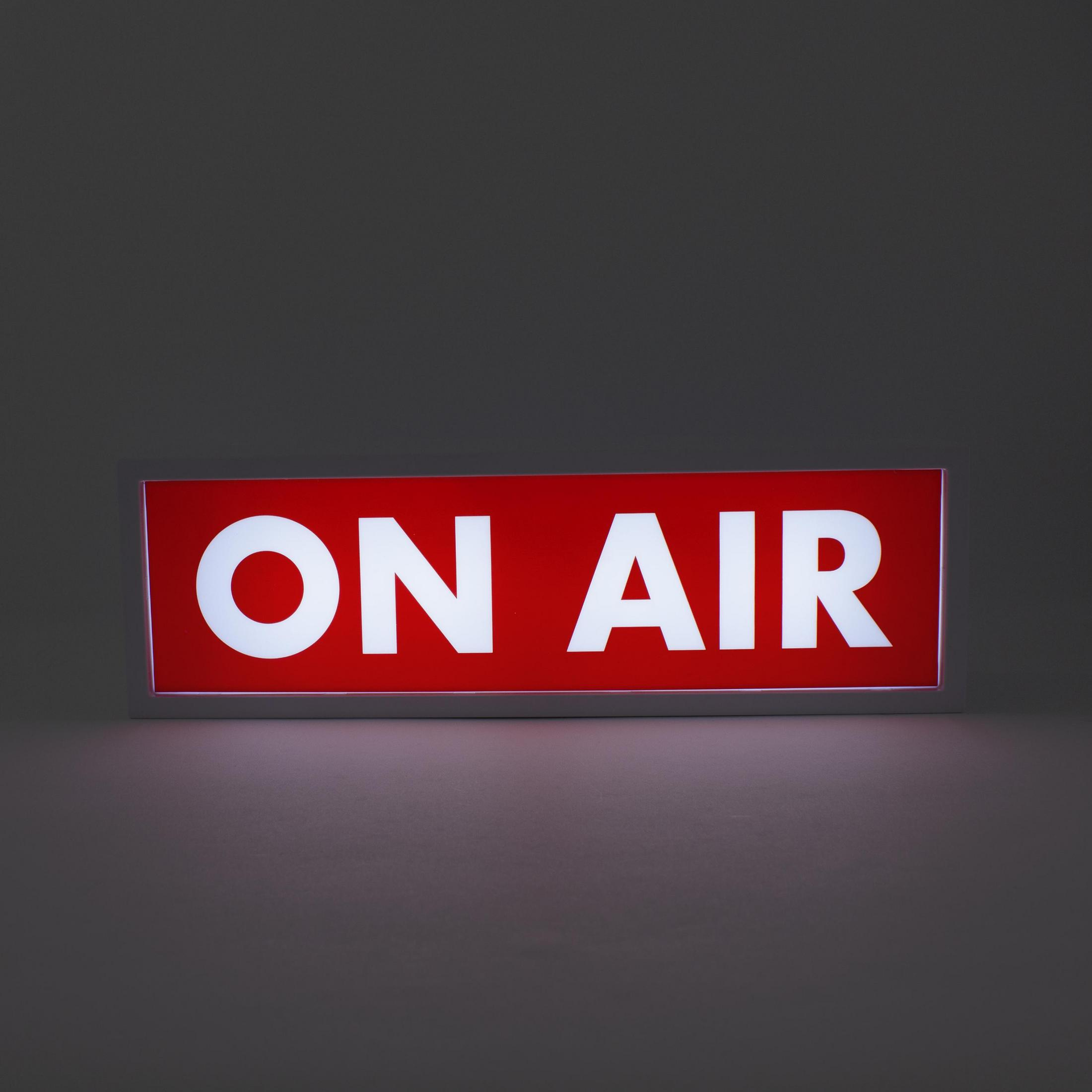 Ein rotes 'ON AIR' Schild mit weißem Text. Das Schild ist in einem weißen Rahmen, vor grauem Hintergrund.