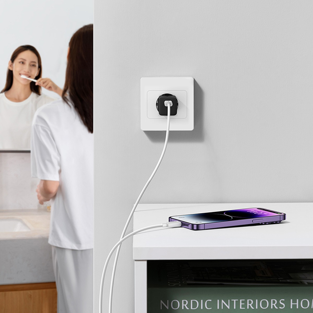 Una donna che si lava i denti mentre un telefono si carica vicino a una presa a muro.