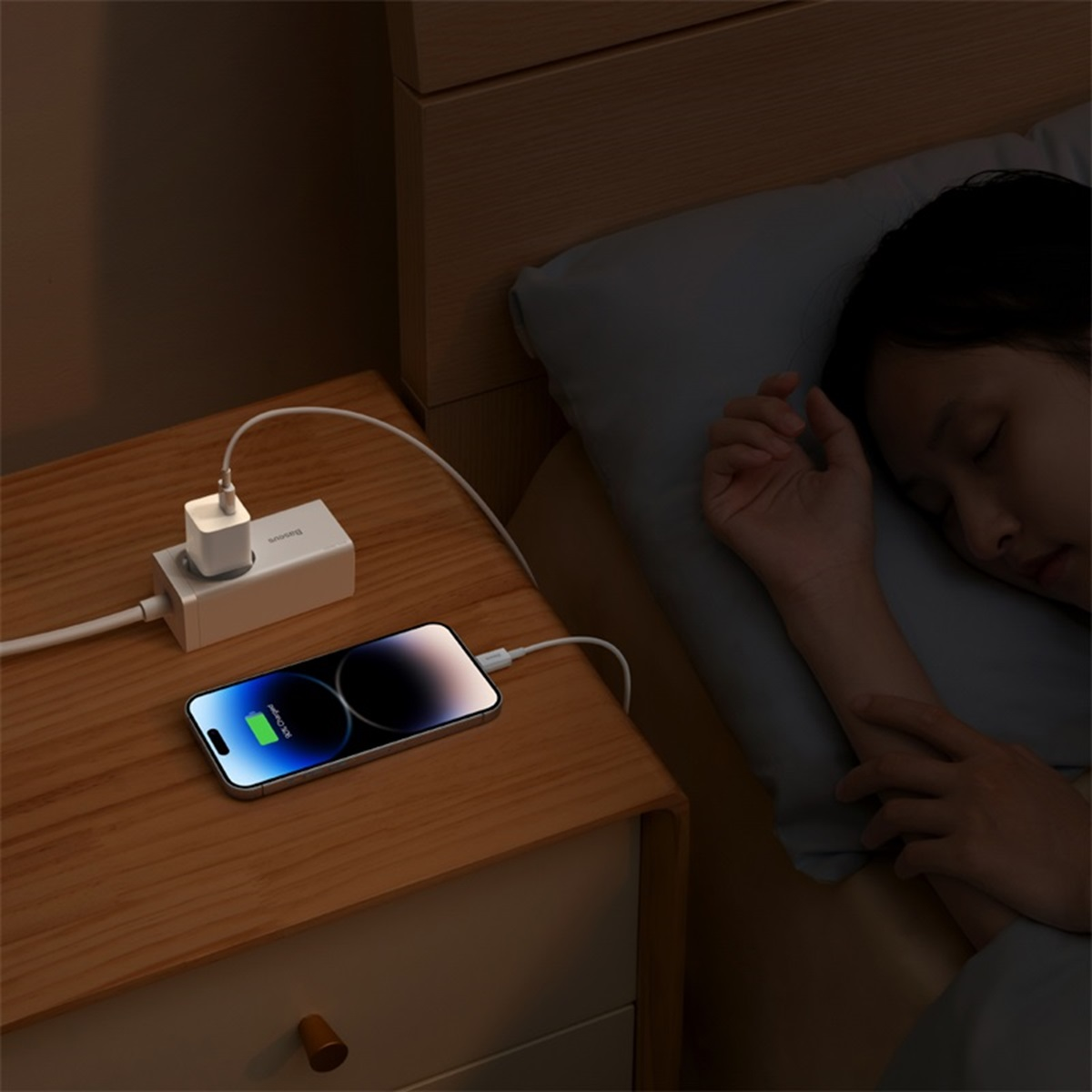 Personne chargeant un téléphone la nuit. Téléphone sur une table en bois. Chargeur blanc. Fond sombre.