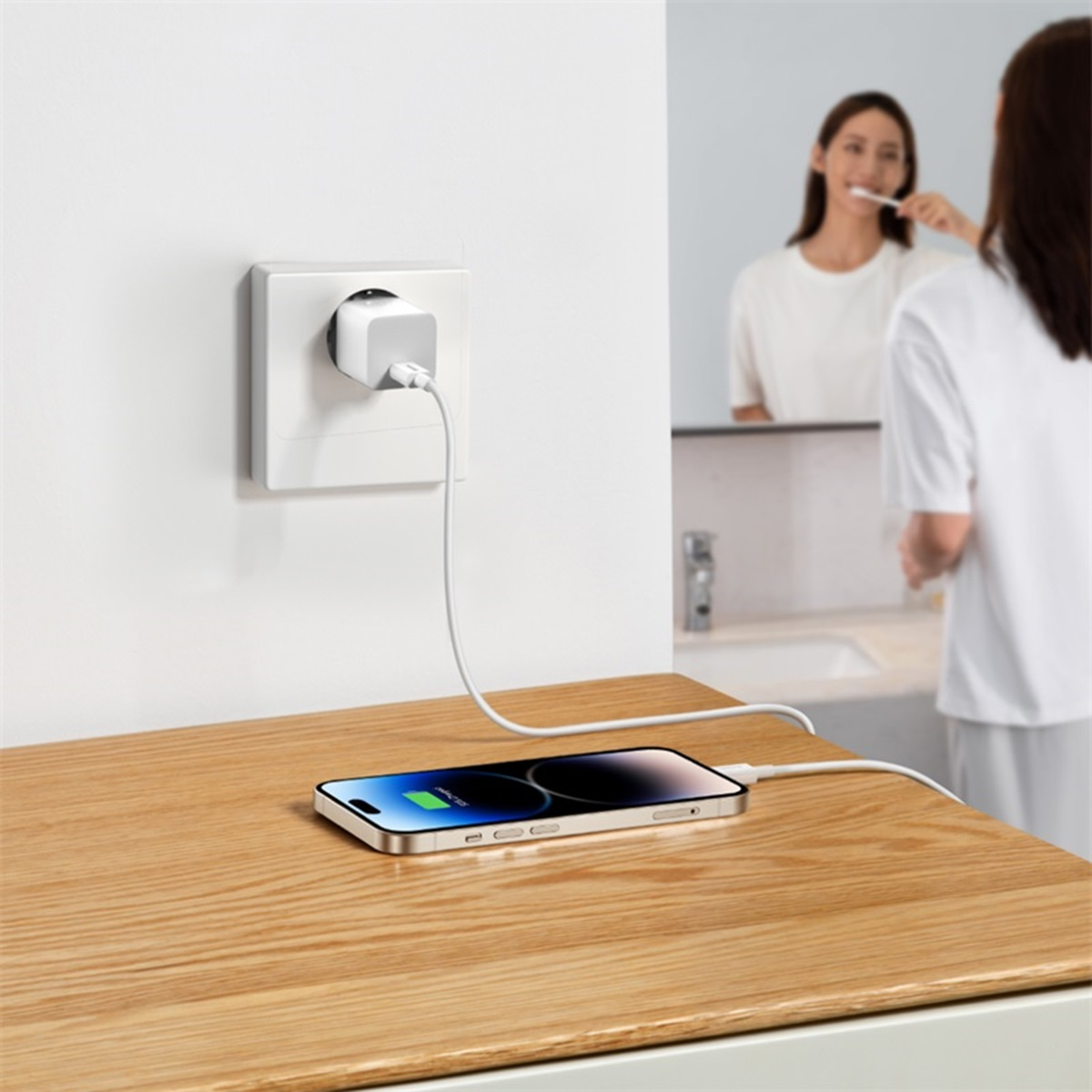 Un téléphone se chargeant sur une table en bois, branché à une prise murale, femme en arrière-plan.