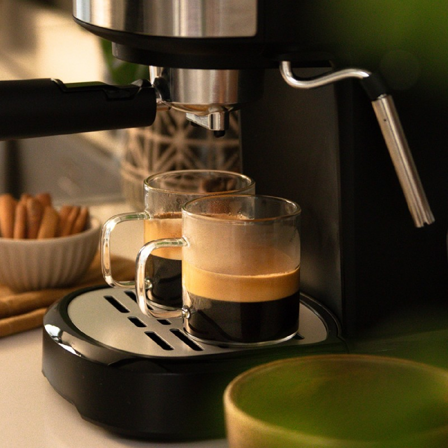 Una máquina de espresso con dos tazas de vidrio llenas de café en la bandeja.