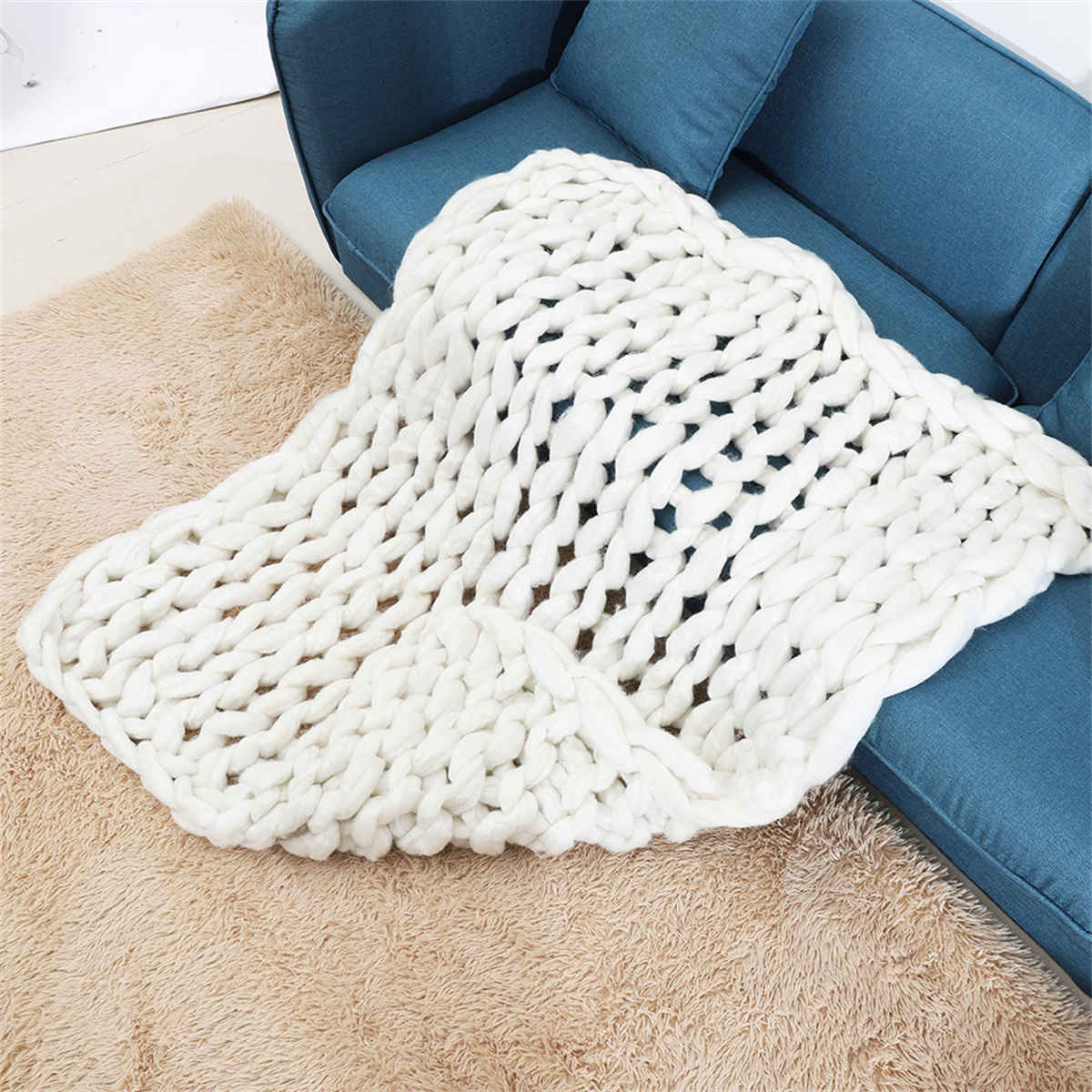 Weiße Strickdecke auf blauem Sofa. Beiger Teppich im Vordergrund. Hintergrund unscharf.
