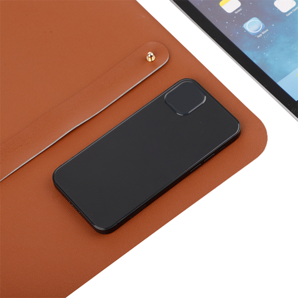 Ein Smartphone, eine braune Ledermatte und ein Tablet. Das Telefon ist schwarz und das Tablet ist im Hintergrund sichtbar.