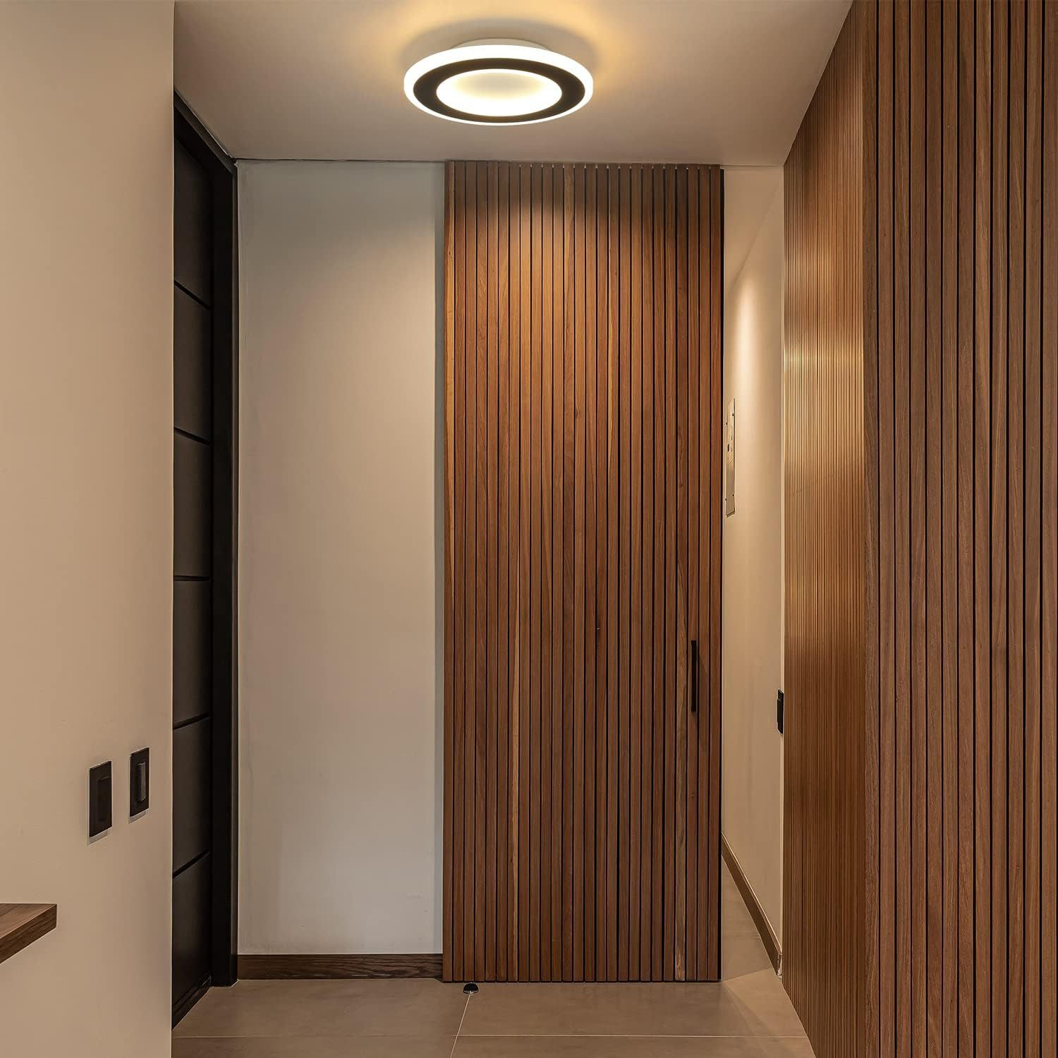 Korytarz z oprawą oświetleniową i boazerią. Pośrodku zamknięte drewniane drzwi.