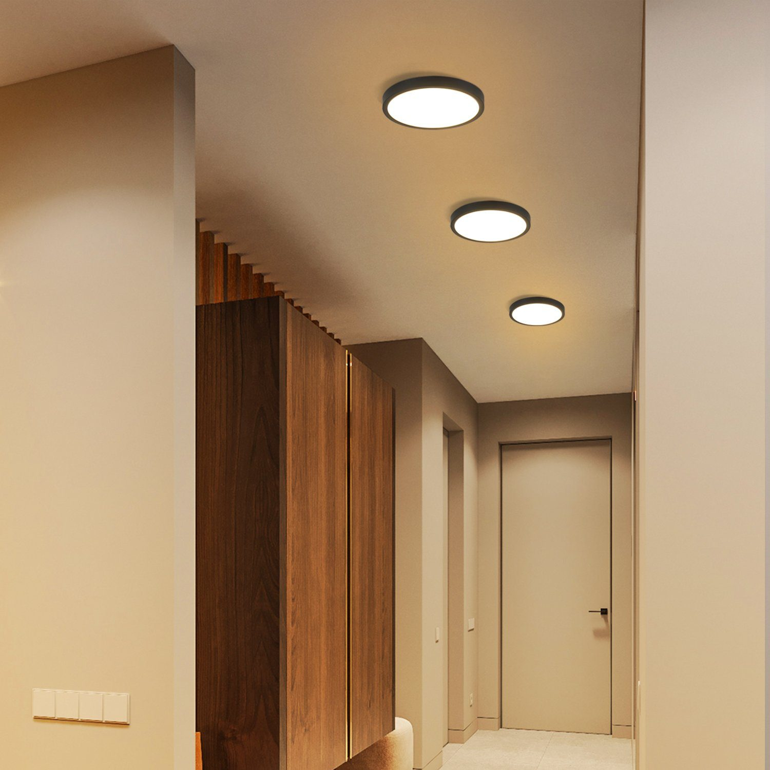 Un corridoio con tre luci a soffitto circolari. Porta in legno e rivestimento a parete a destra.