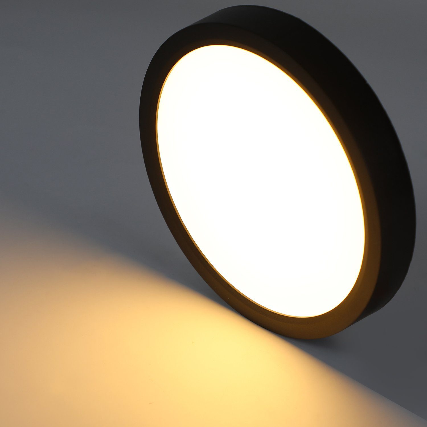 Lampada rotonda nera con luce bianca e ombra. Sfondo grigio.