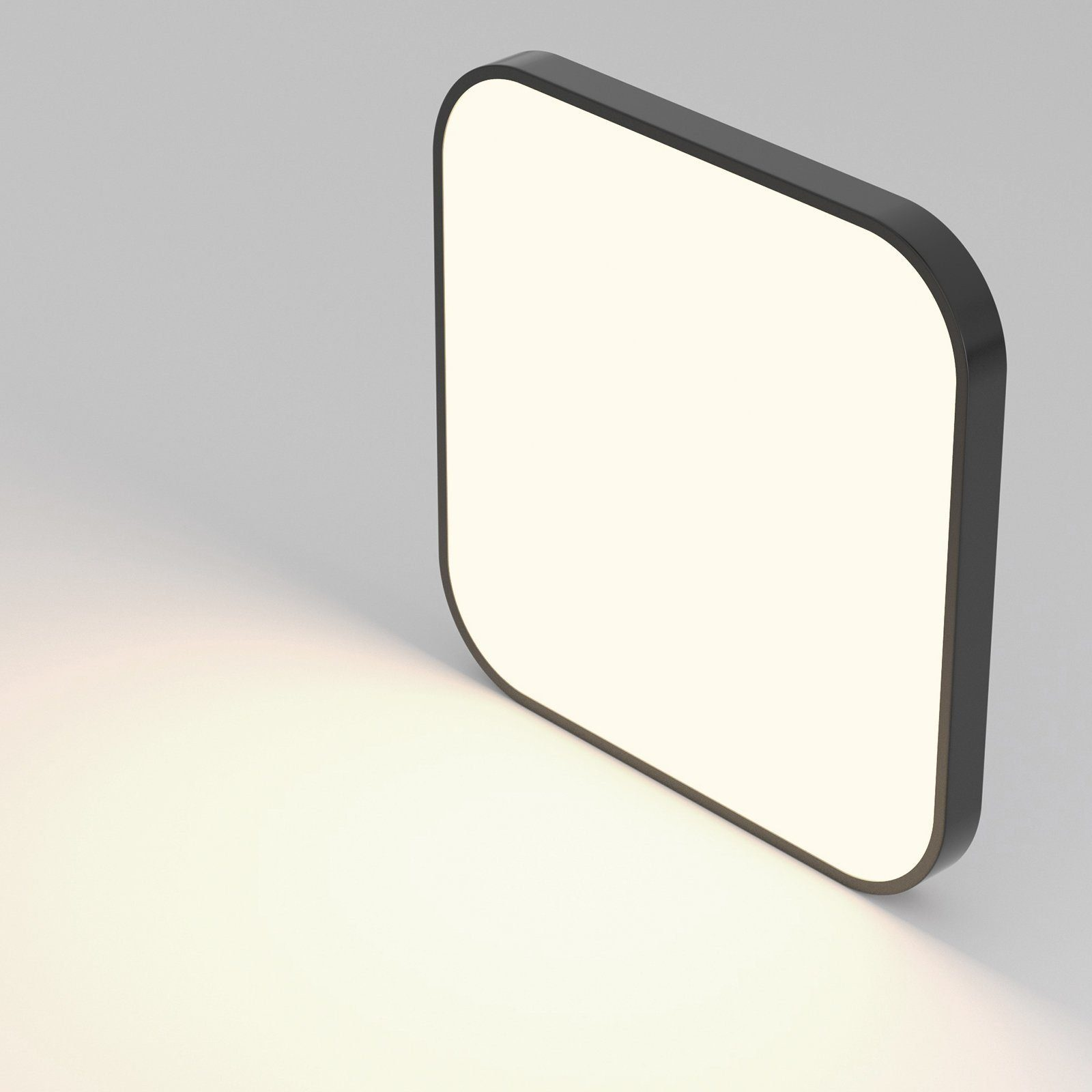 Czarna, kwadratowa lampa z jasnym, białym wnętrzem na szarej powierzchni.