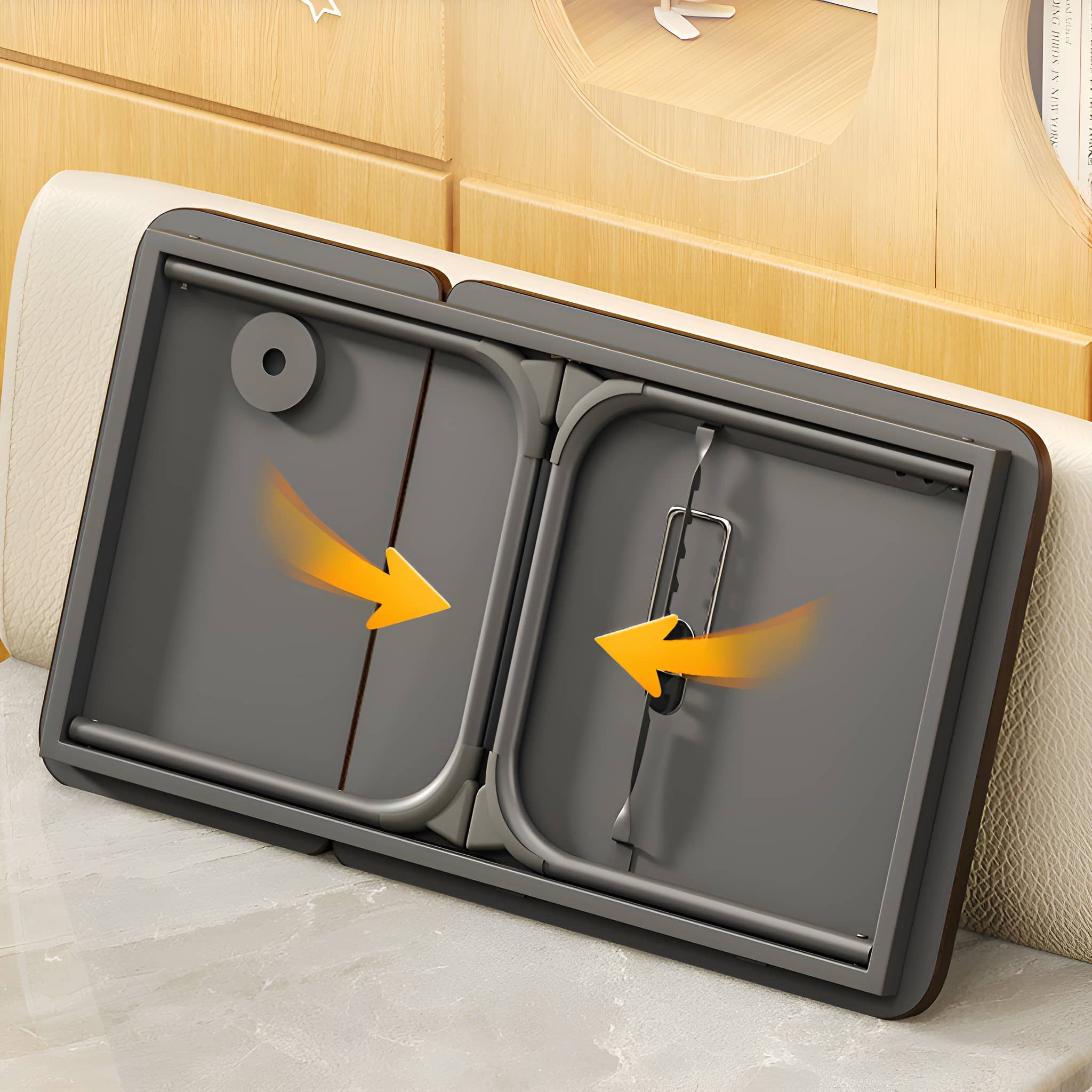 Klappbarer grauer Tisch auf einem Bett. Orangefarbene Pfeile zeigen die Faltrichtung.