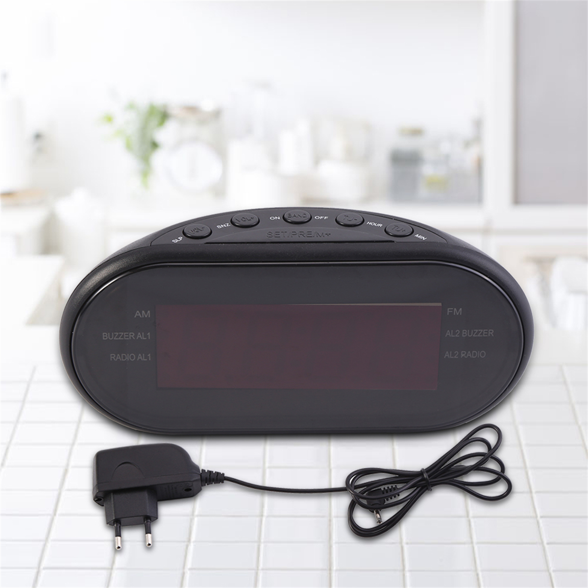 Schwarzer ovaler digitaler Wecker mit Display und Netzteil auf einer Oberfläche.