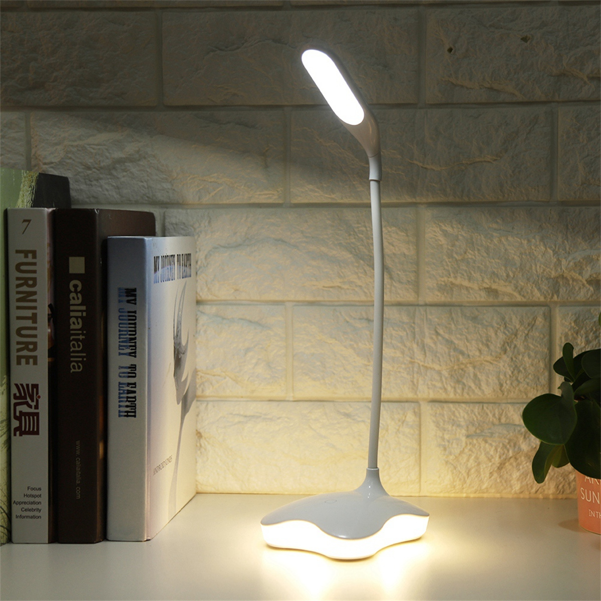 Weiße Schreibtischlampe auf einem Schreibtisch mit Büchern. Die Lampe ist an und leuchtet.