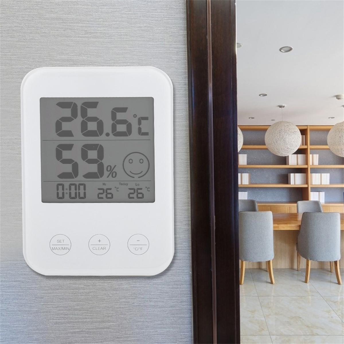 Eine weiße Digitaluhr, die Zeit und Temperatur anzeigt, im Hintergrund ein Raum.