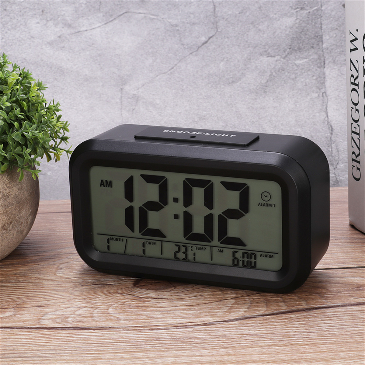 Schwarzer digitaler Wecker mit Anzeige von Zeit, Datum und Temperatur auf Holzoberfläche.