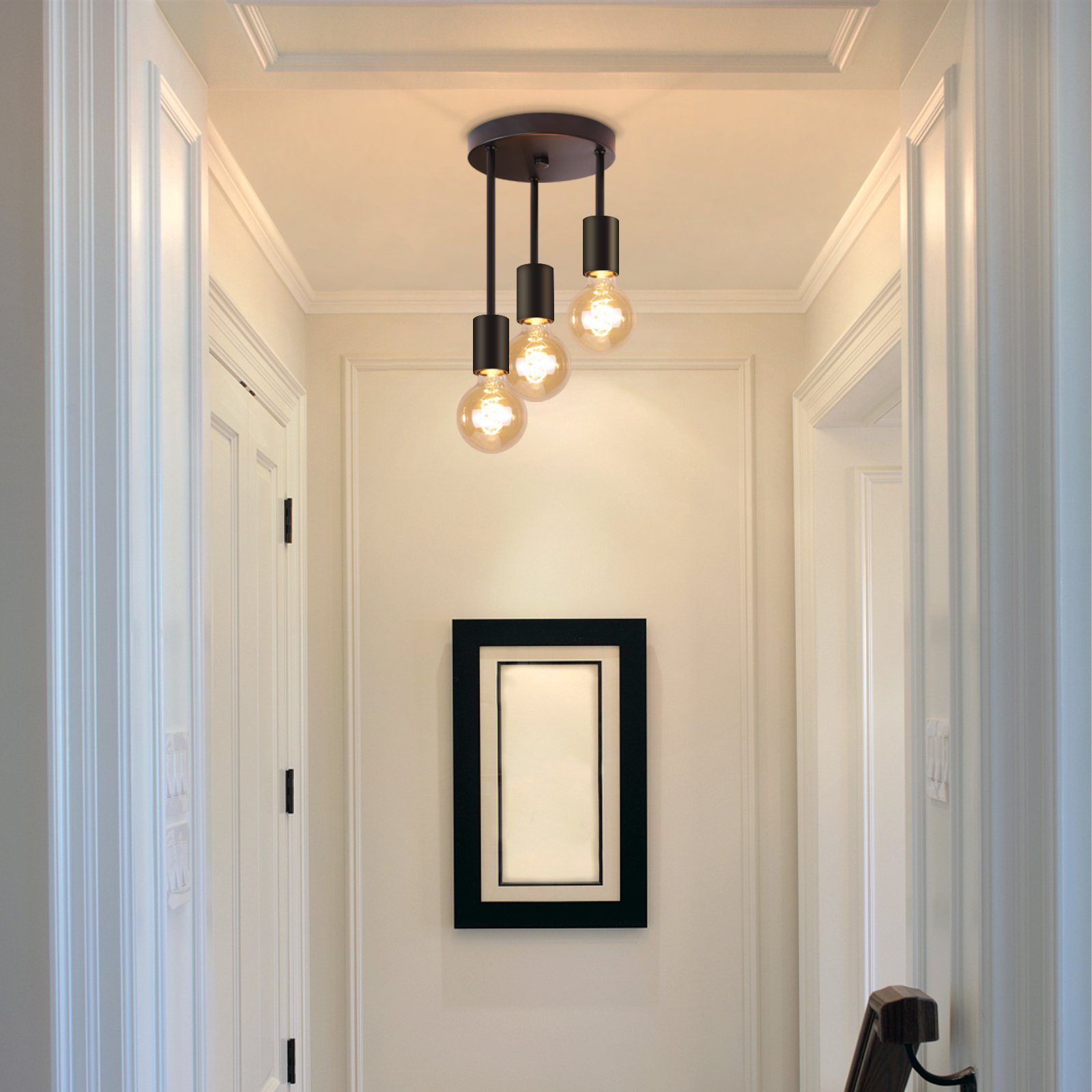 Korytarz z wiszącą lampą i obrazem w ramie. Białe ściany i drzwi. Jasna drewniana podłoga.