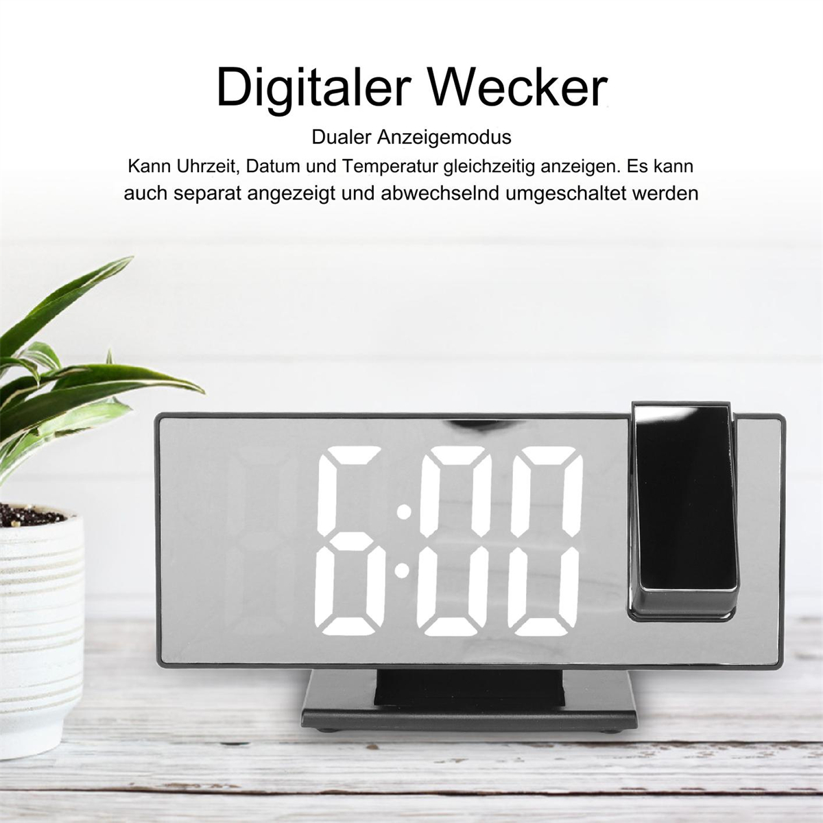 Digitaler Wecker mit weißen Ziffern. Es zeigt 6:00 Uhr an. Pflanze in der Ecke.