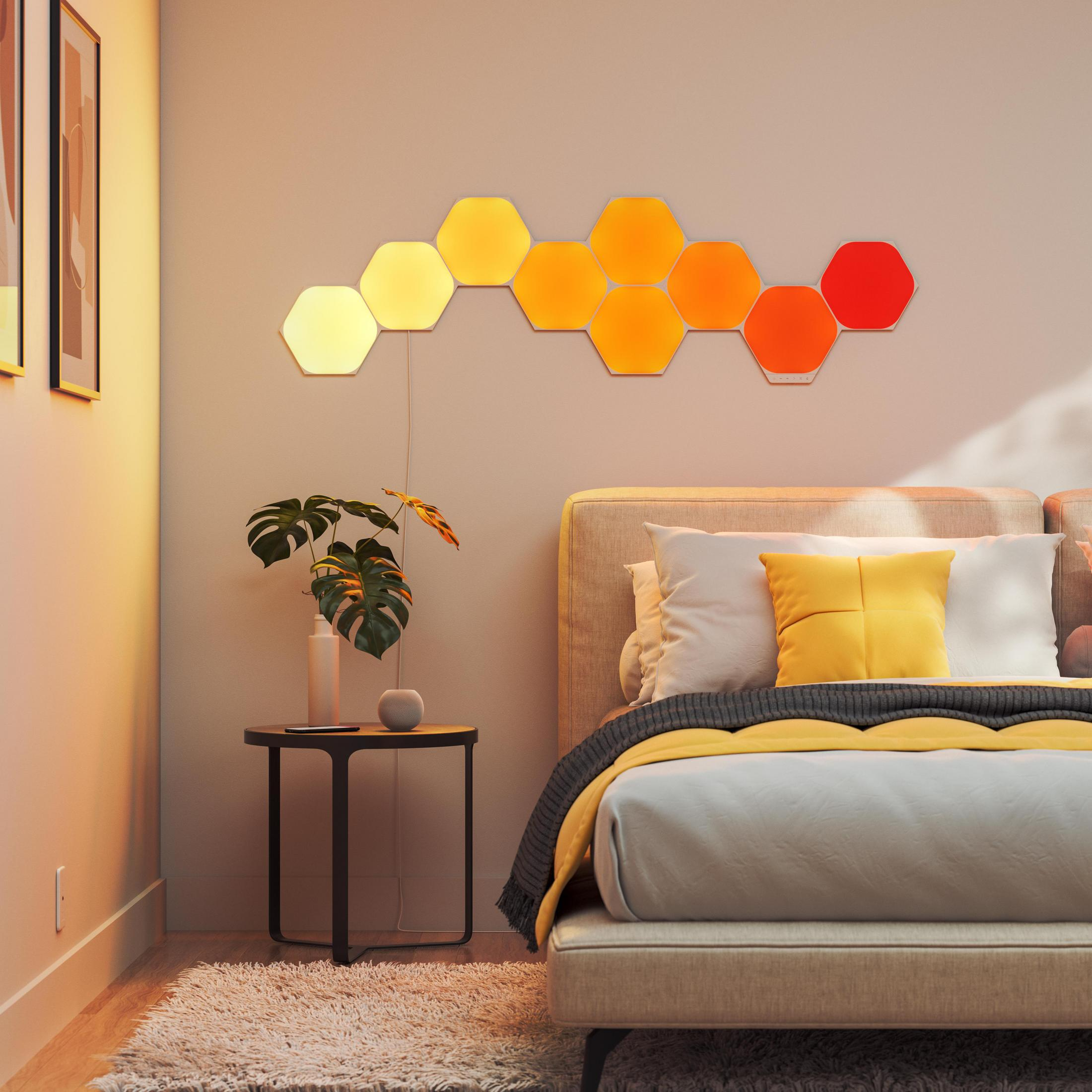 Schlafzimmer mit Honigwabenlichtern an der Wand, Bett und Beistelltisch mit Pflanze.