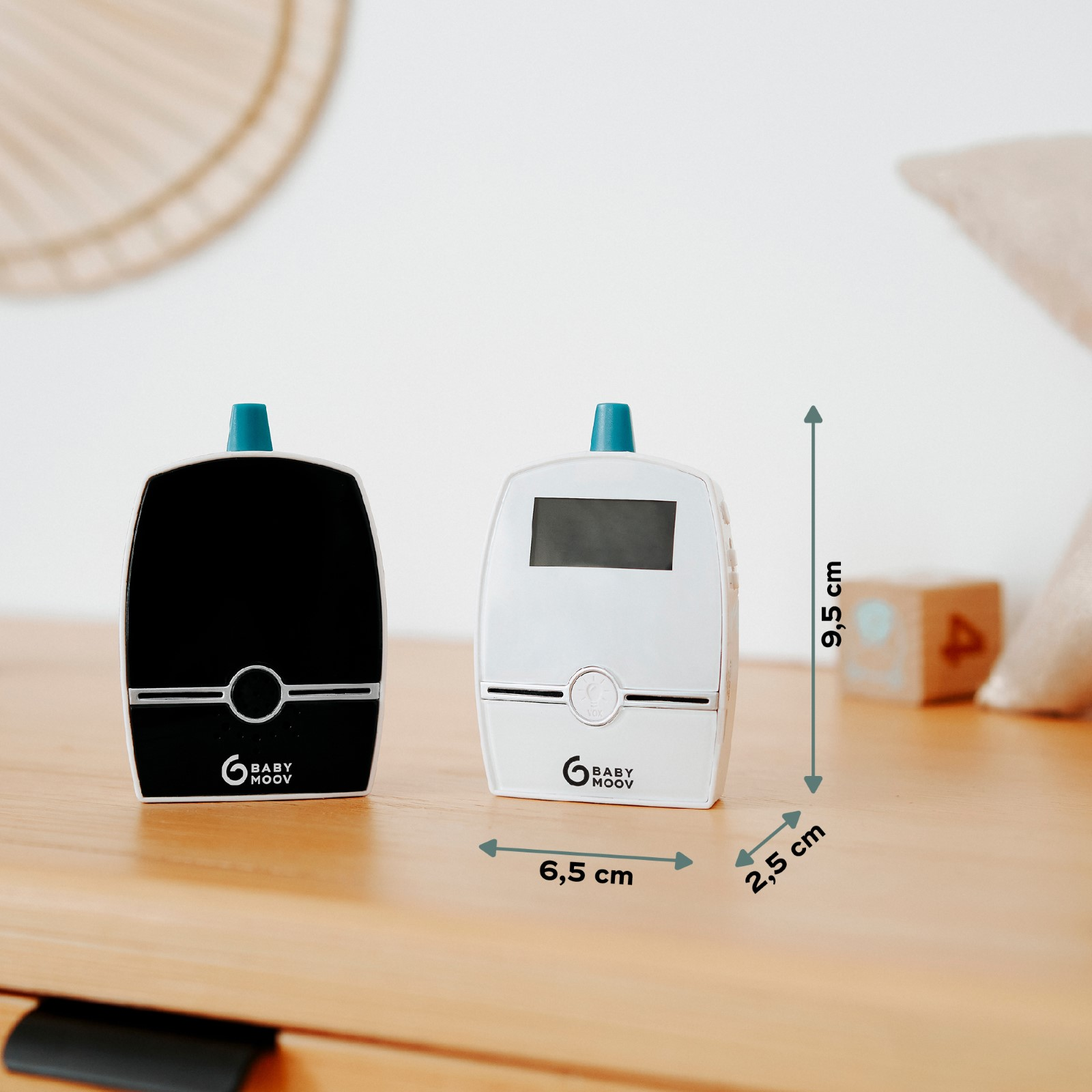 Zwei Babyphone, eines schwarz und eines weiß, auf einer Holzoberfläche. Abmessungen werden angezeigt.