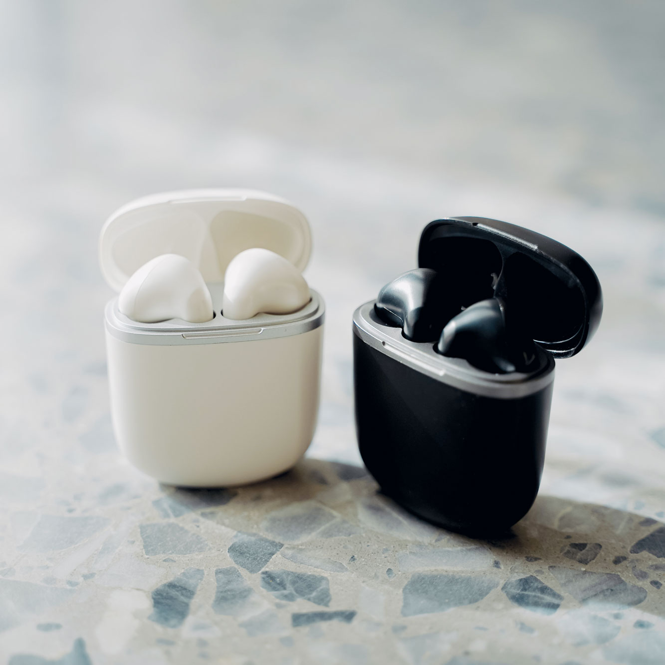 Twee draadloze oortelefoons in hun oplaadcases. Eén wit, één zwart, op een marmeren oppervlak.